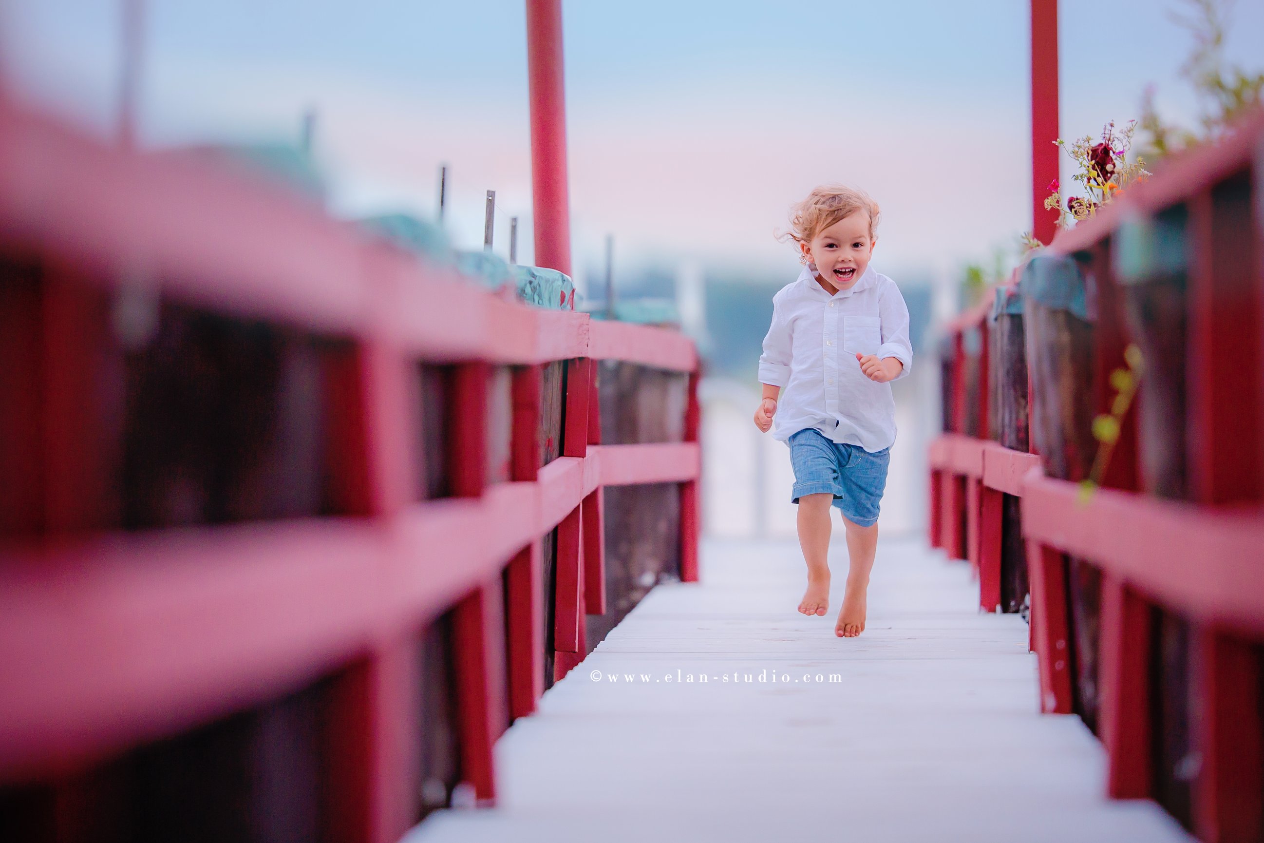 little boy in white button-down shirt and blue shorts running on red dock