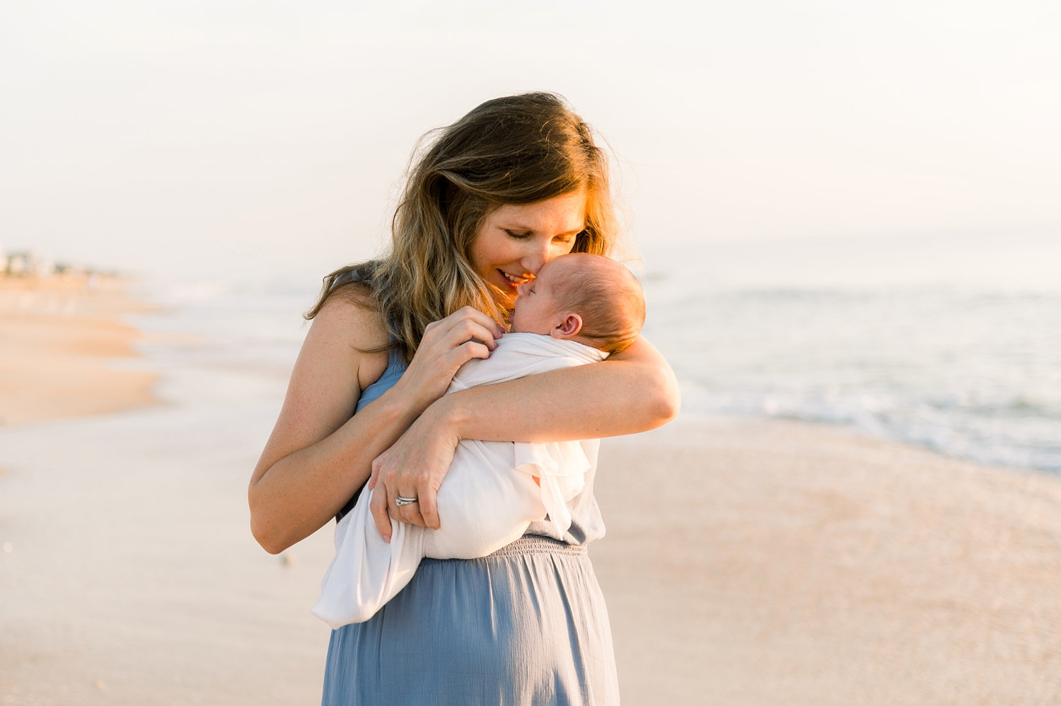 mother holding her newborn baby, the baby is swaddled in a simple white cloth, sunrise at Ponte Vedra Beach