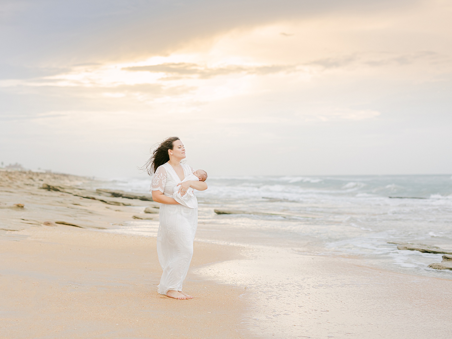 woman standing on beach in st. augustine Florida holding newborn baby at sunset