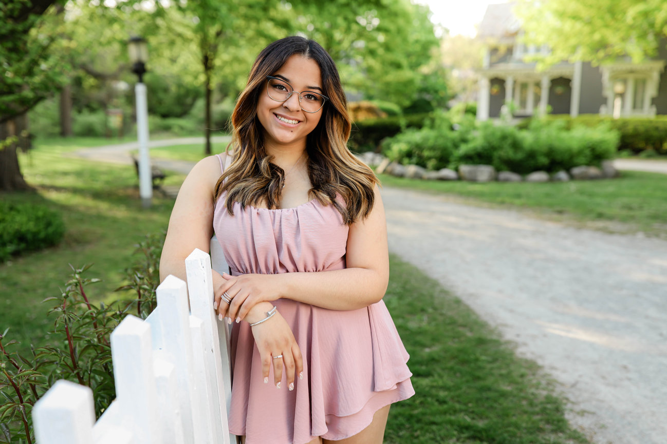 High school senior girl with long hair posing by white picket fence