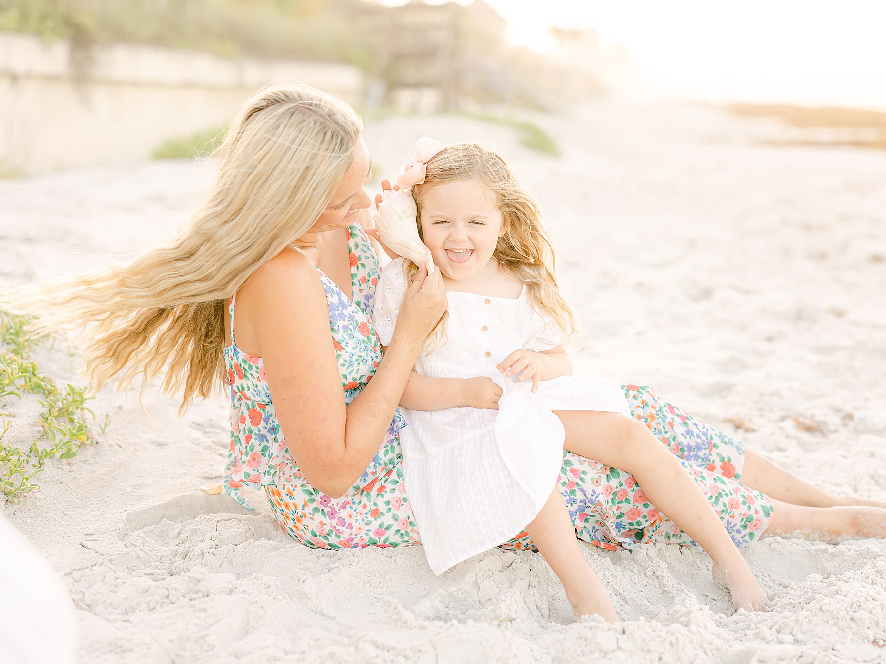 mom and girl laughing holding seashell on the beach in dresses
