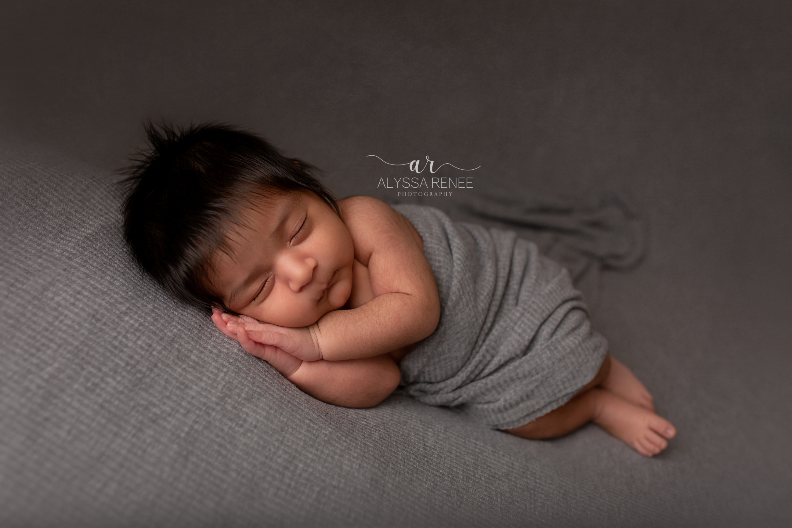Beautiful artistic newborn portrait on gray blanket with loose swaddle