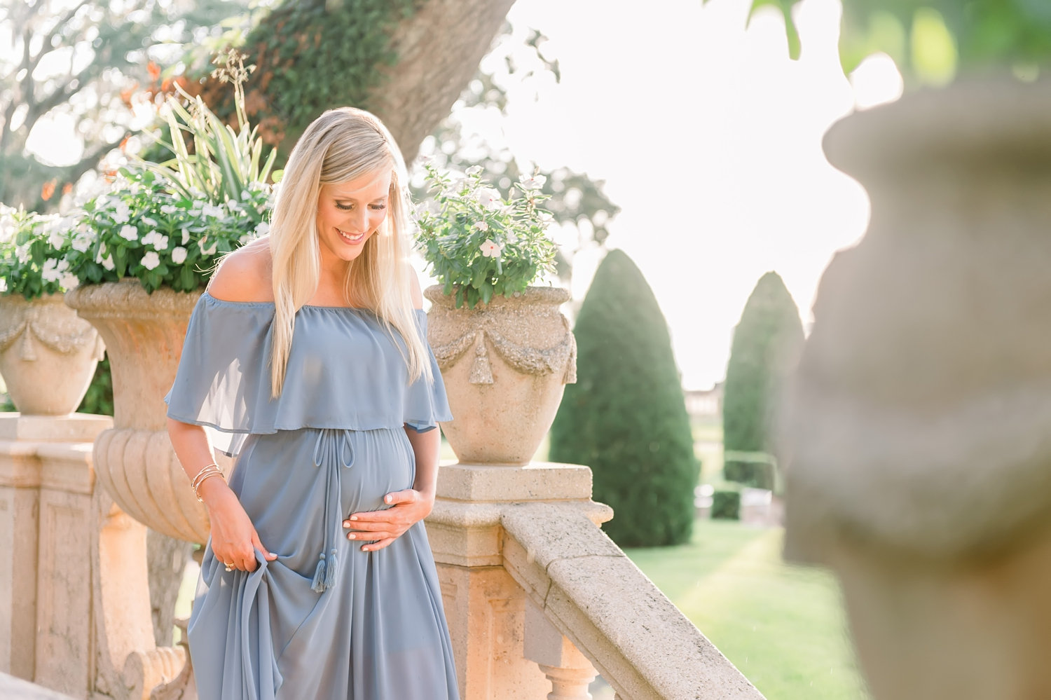 pregnant mother to be with long blonde hair, she is wearing a strapless light blue gown, beautiful manicured garden grounds