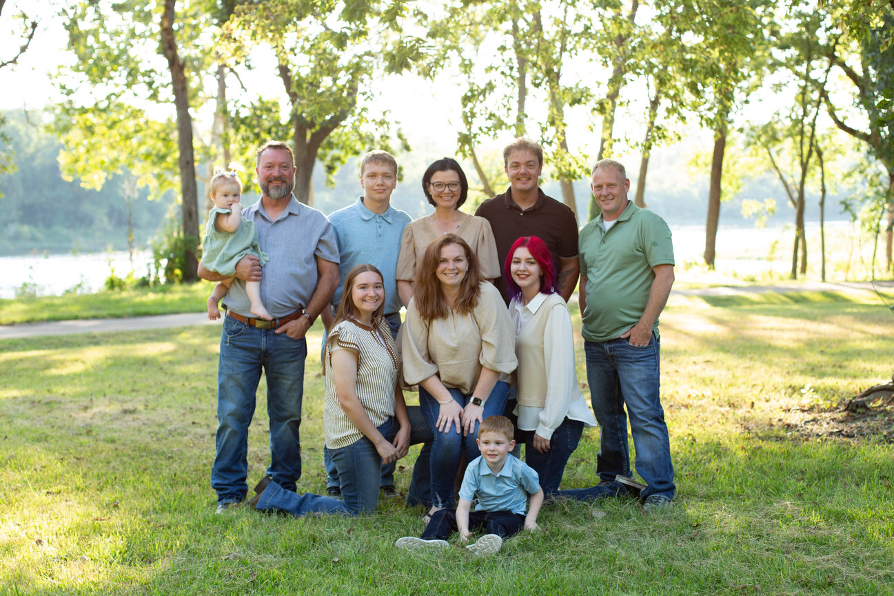 Large family posing together under trees in a sunlit park.
