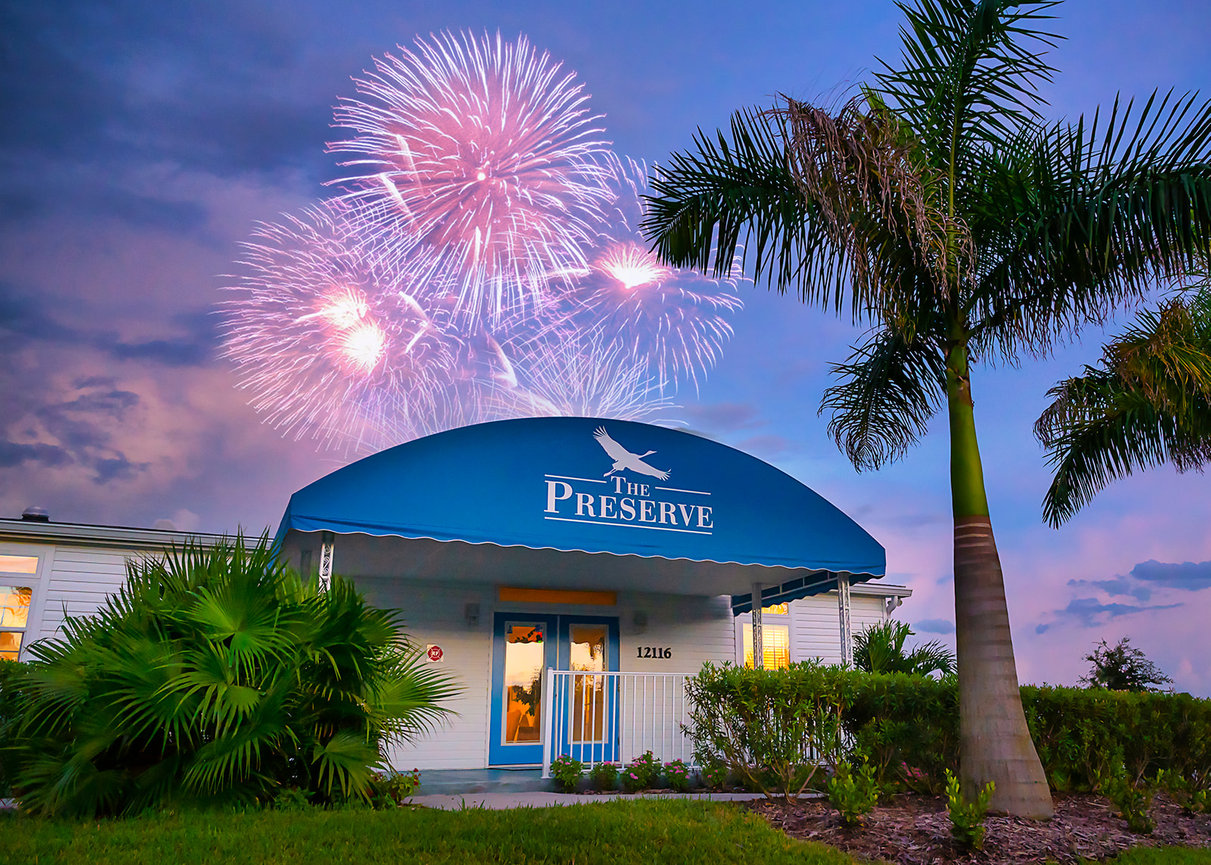 Fireworks over The Preserve building at twilight, surrounded by palm trees and lush landscaping.
