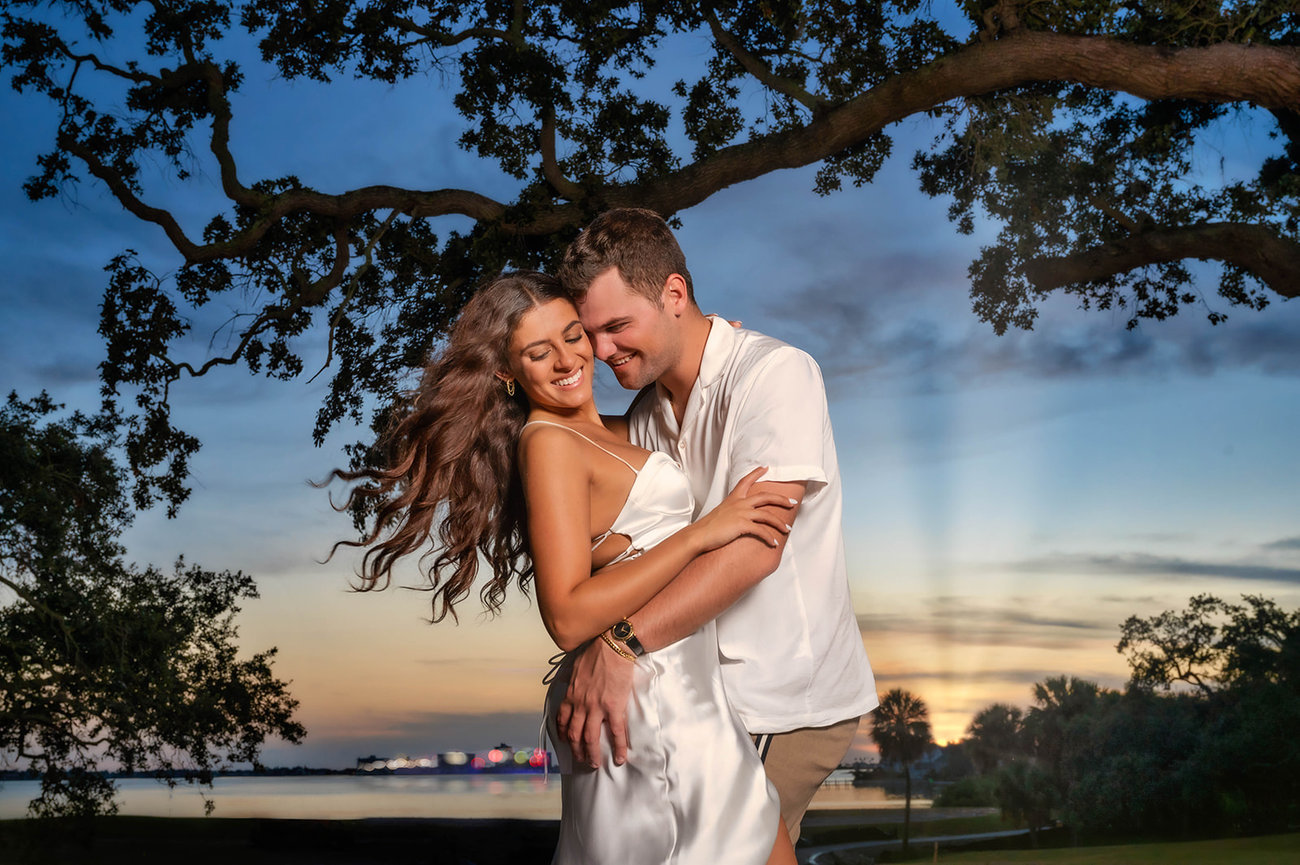 Couple sharing a joyful moment outdoors at sunset, surrounded by trees and a scenic background.