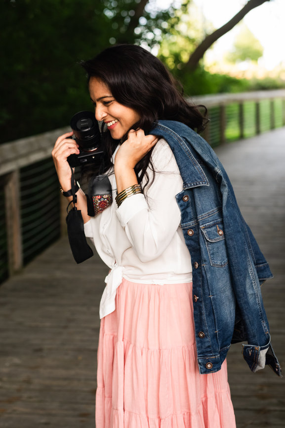 female entrepreneur photographer stands sideways laughing with camera and jean jacket on wooden bridge in clarkston park