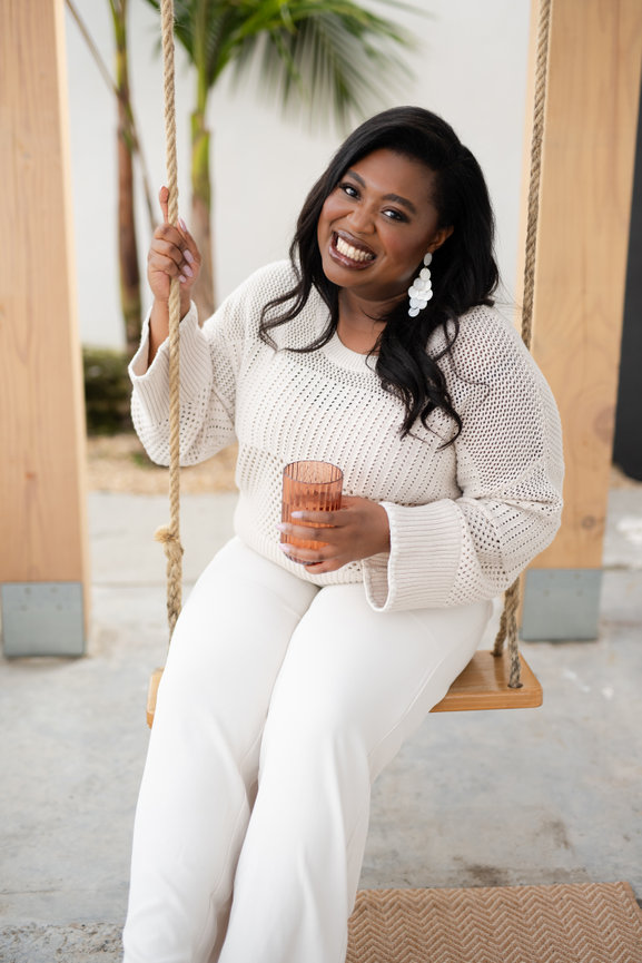 small business owner web designer smiles on outdoor swing with cocktail for lifestyle headshot during personal brand session
