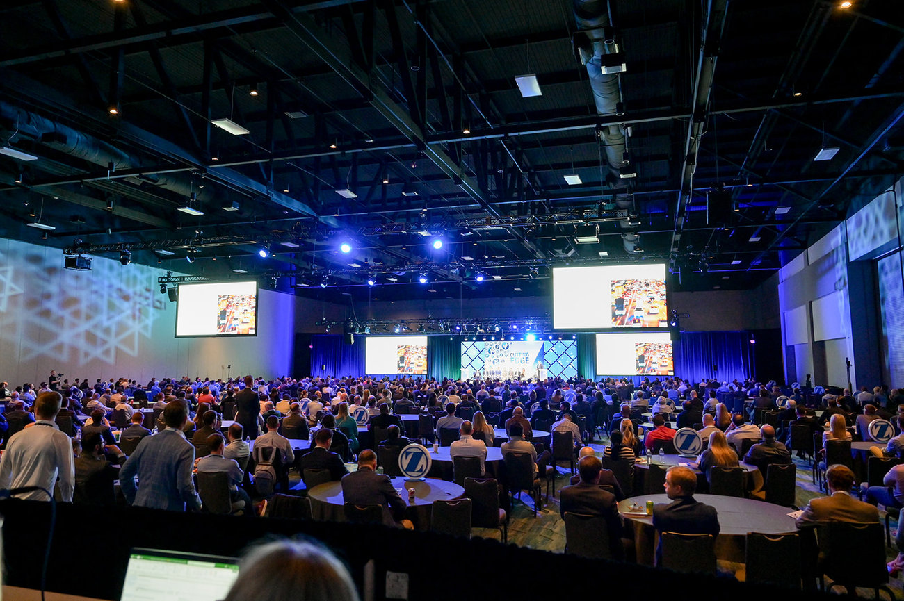Large conference setting with a captivated audience and multiple screens displaying a presentation.