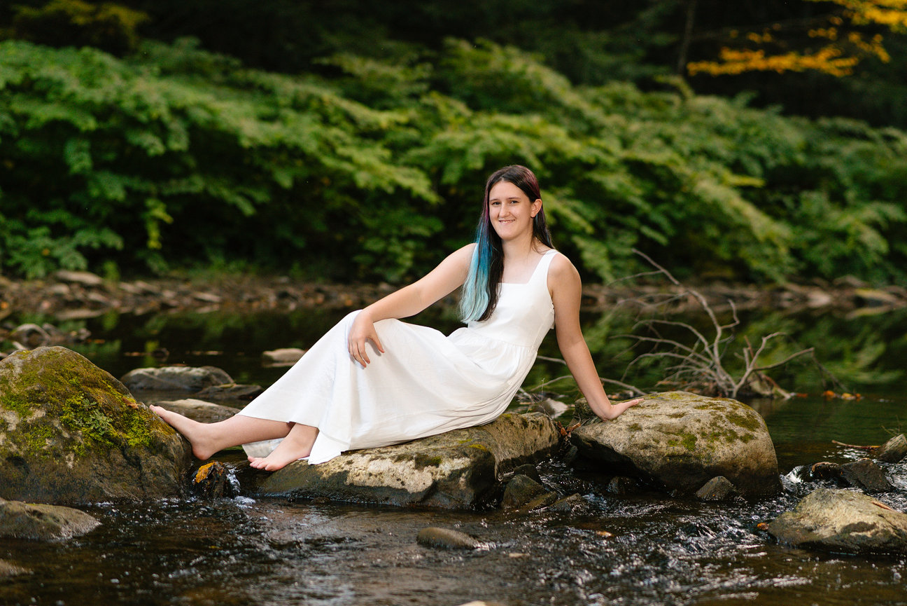senior girl in a white dress sitting in a creek