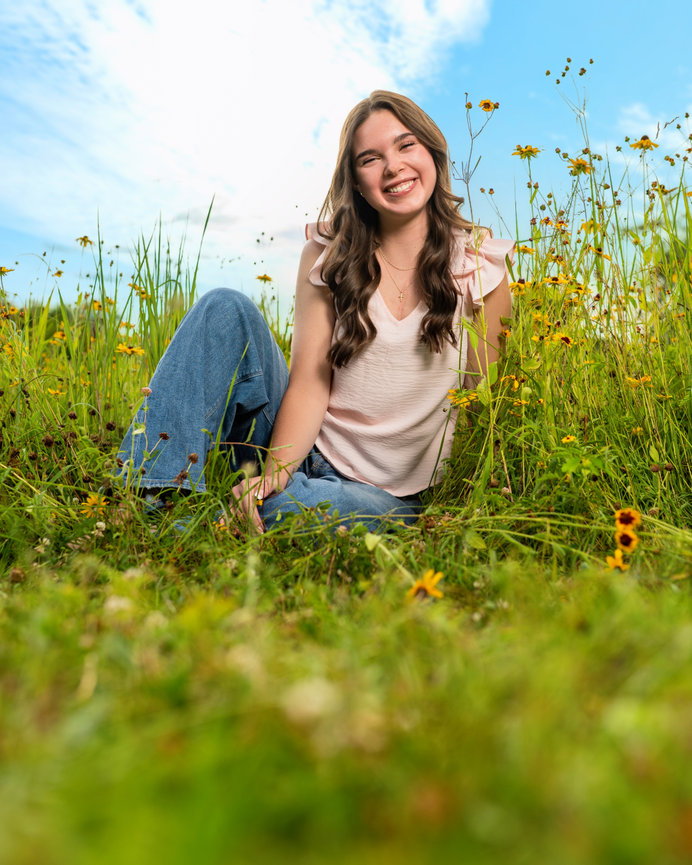 senior girl wearing jeans and a cute top smiling in a flower field