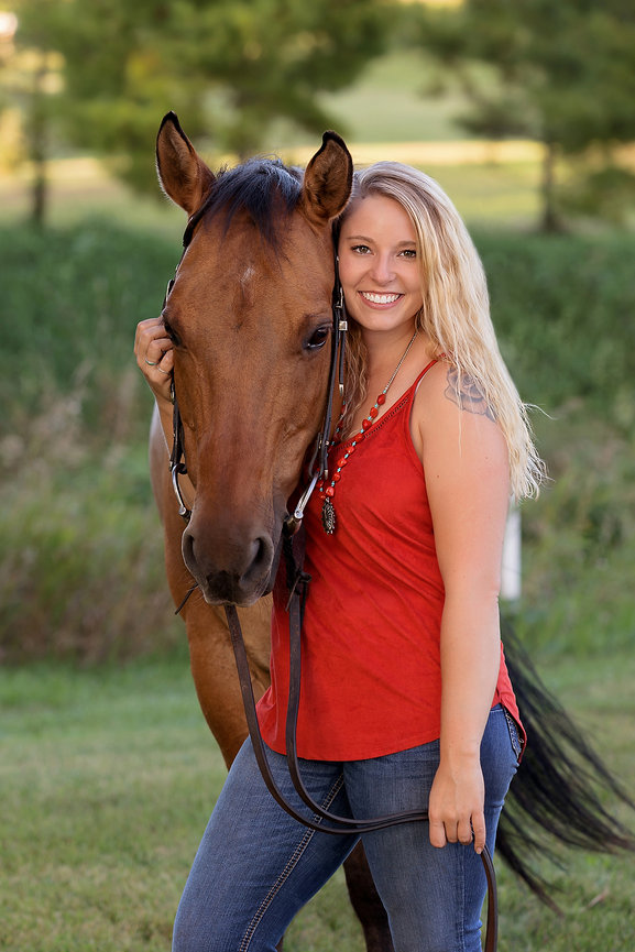 Woman smiling with a brown horse in a grassy outdoor setting.