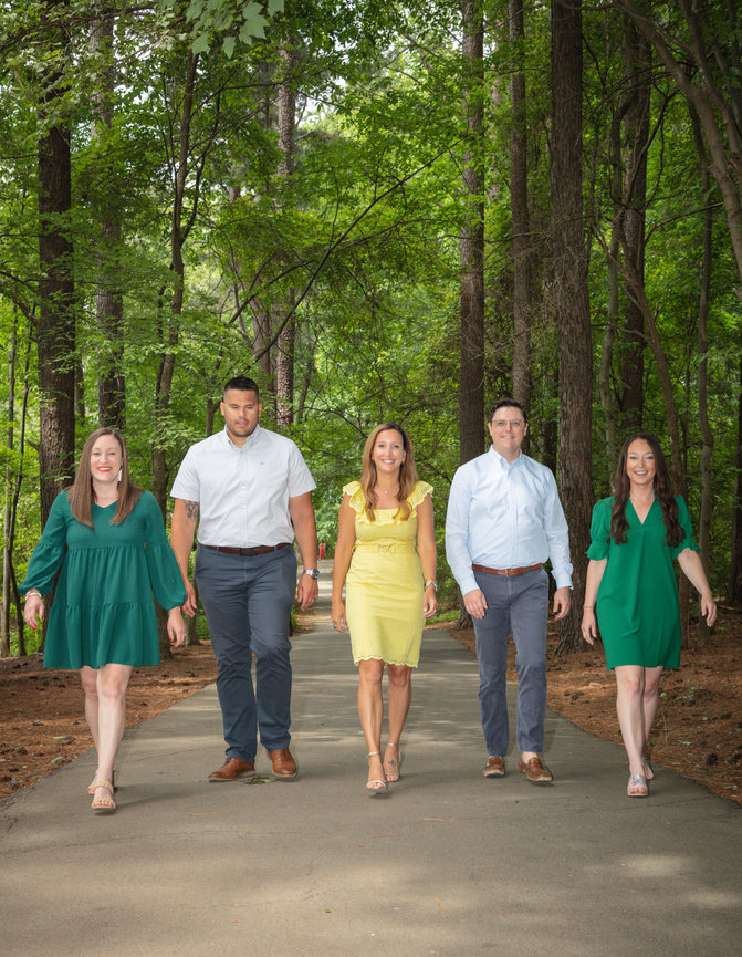 Five people walking on a path in a forest, dressed in casual attire.