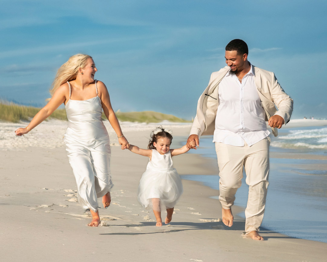 Bride and groom running hand in hand with their daughter along the shoreline during a joyful family beach elopement along the Gulf Coast! captured by wedding photographer Dixon Creative Images.