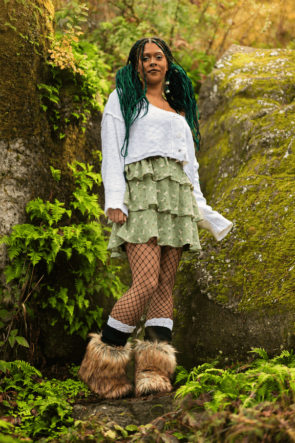 Person standing on a mossy forest path in a layered outfit and boots.