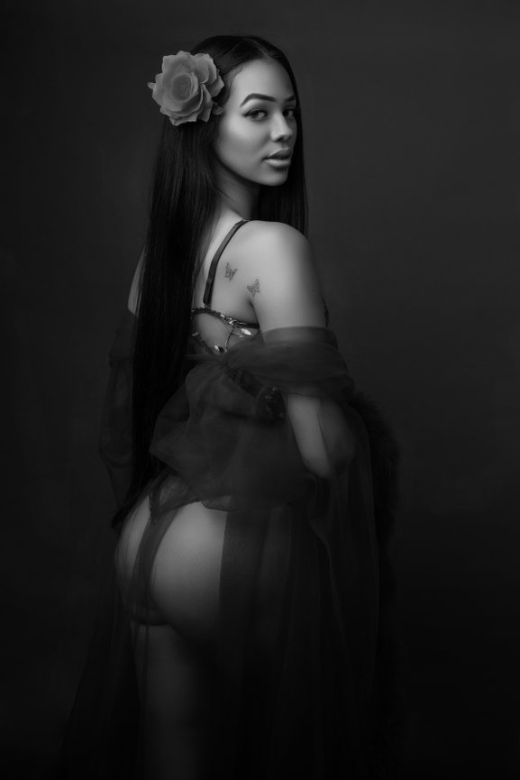 Glamorous woman in dark lingerie, softly lit against black.