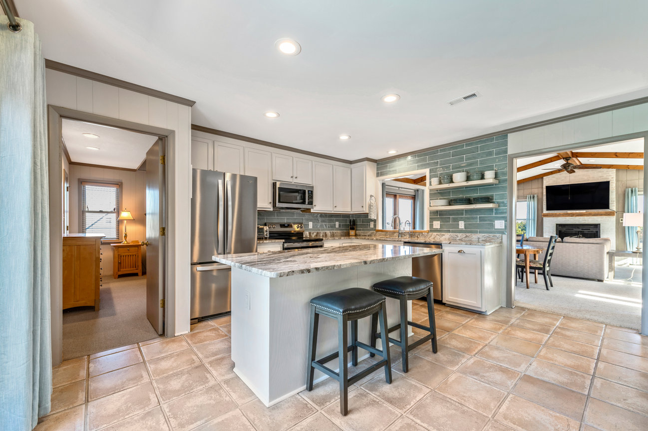 Modern kitchen with marble countertops, stainless steel appliances, and tile flooring. Adjacent room with fireplace visible.