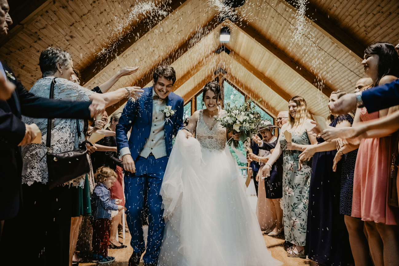 Bride and groom walk down a rustic aisle as guests cheer on both sides.