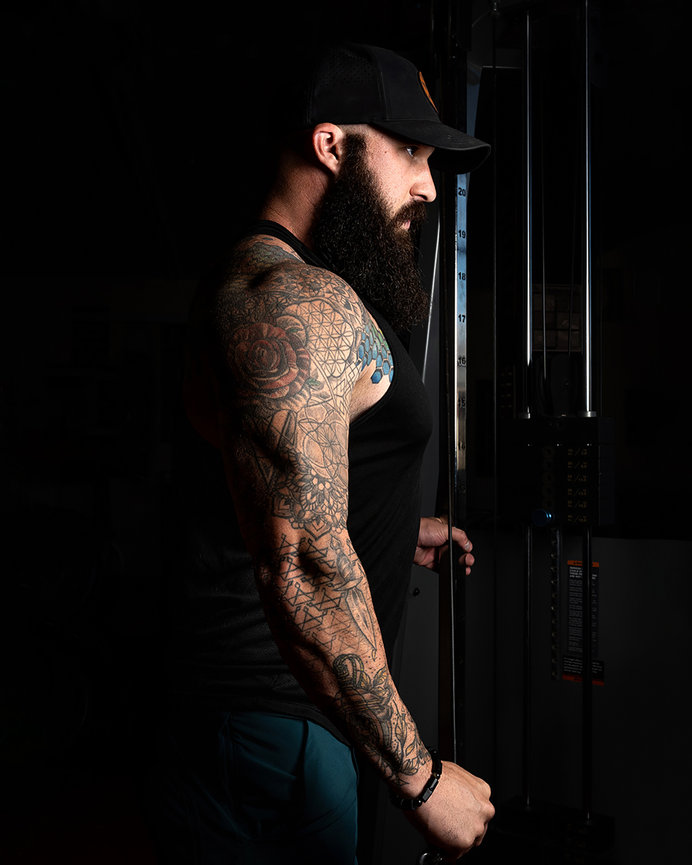 Tattooed fitness enthusiast with a beard performing strength training at Rage Fitness in Lehi, Utah. Captured by Tre Nelson Photo, specializing in fitness photography and personal branding.