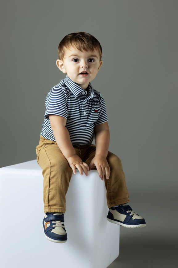 Toddler in grey polo shirt on a white block