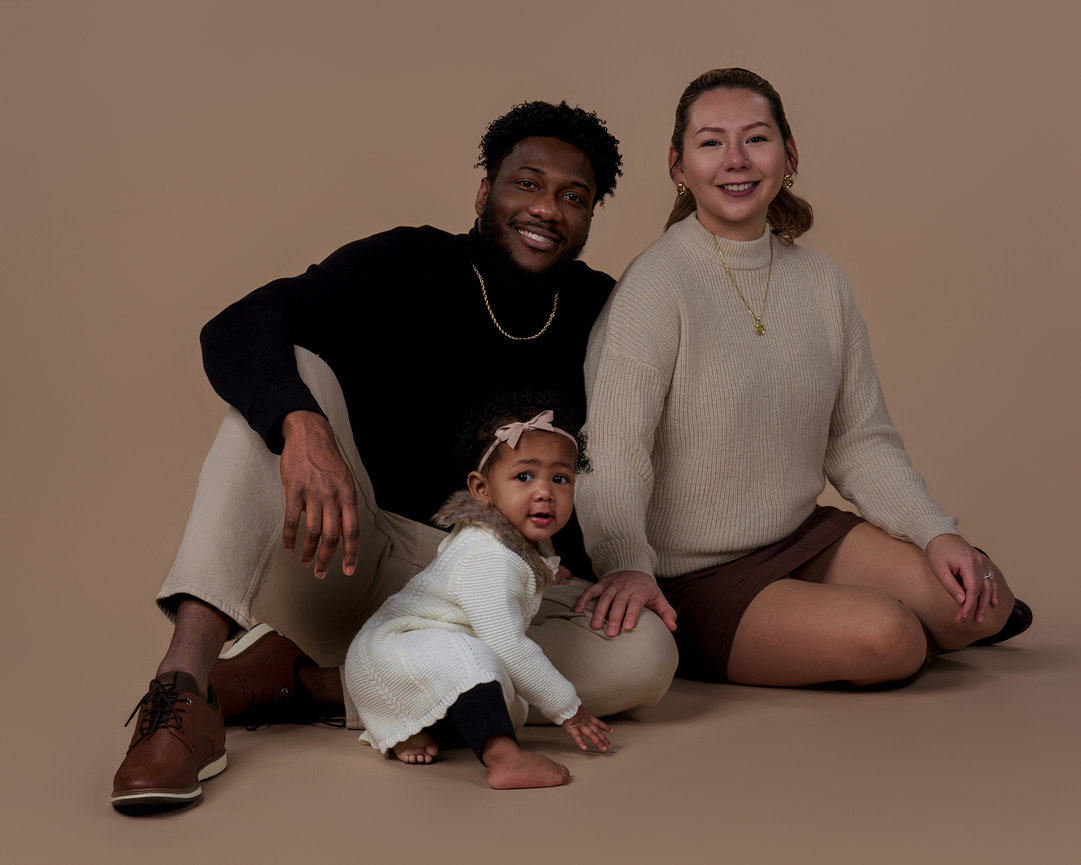 Studio portrait of a young family with a toddler sitting on a neutral background, photographed by a Sherman TX family photographer