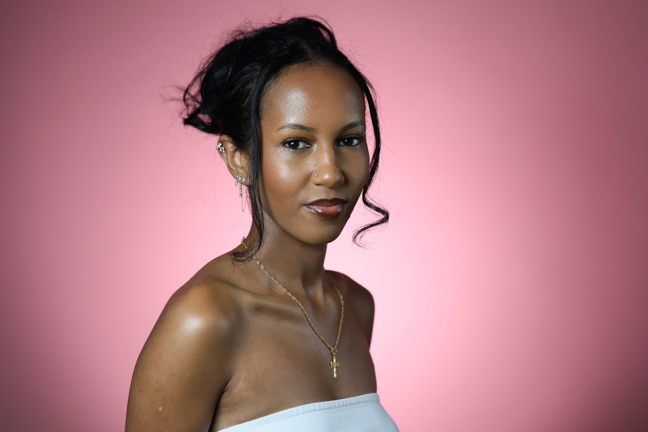 Portrait of a woman against a pink background wearing a white top.
