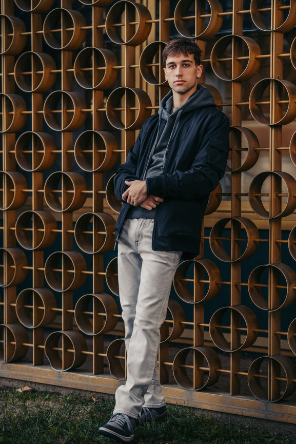 Young man posing against a decorative metal wall in urban setting