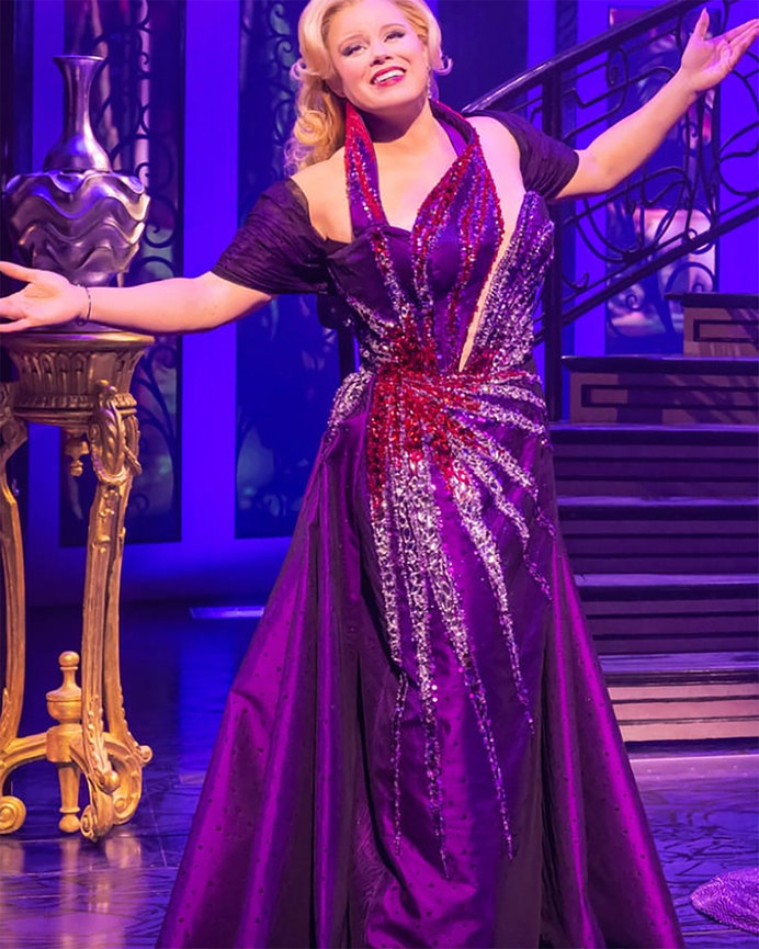 Singer in a sparkling purple gown posing on a stage with purple lighting.