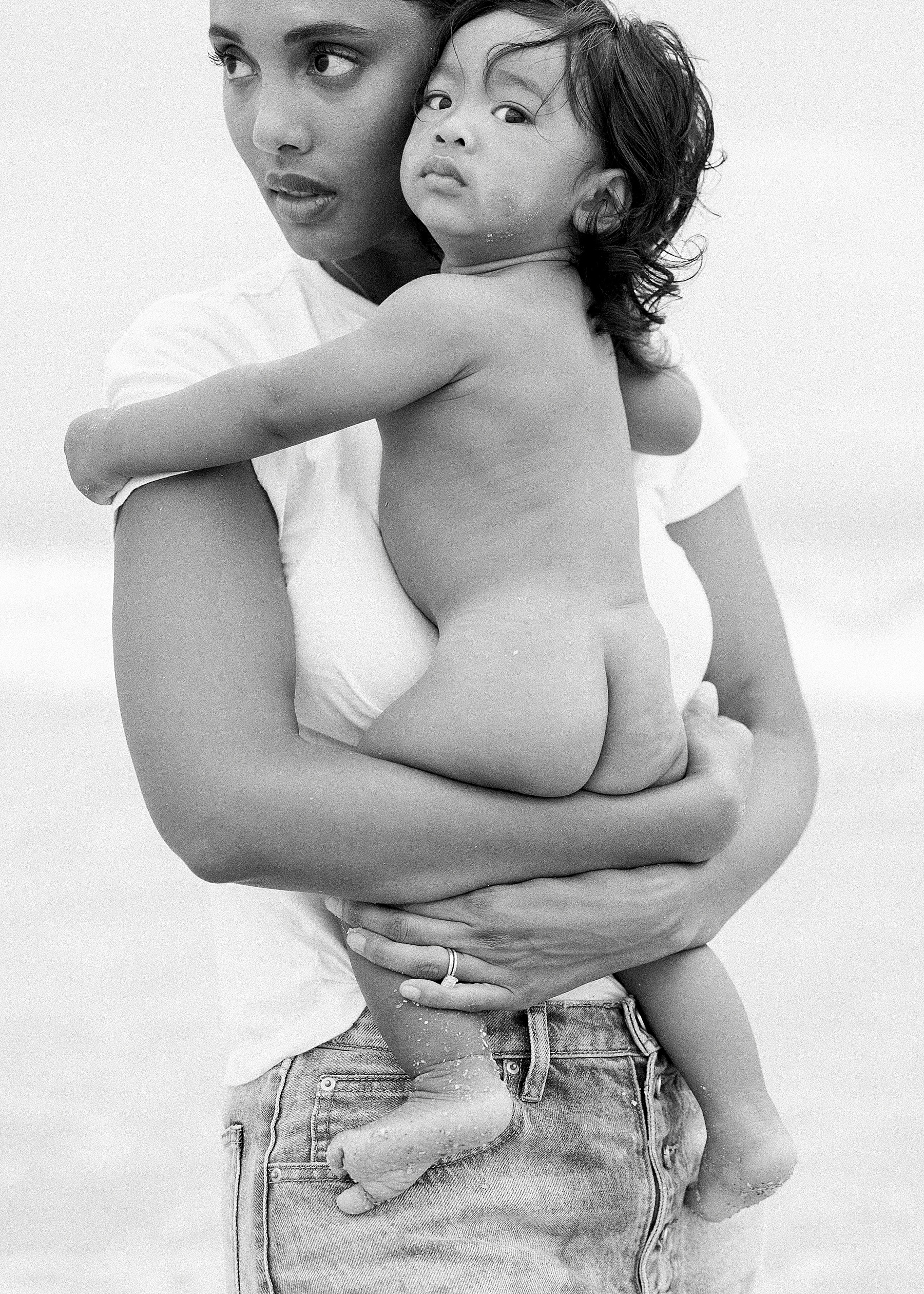 mom holding baby wearing white shirt and jeans on the beach