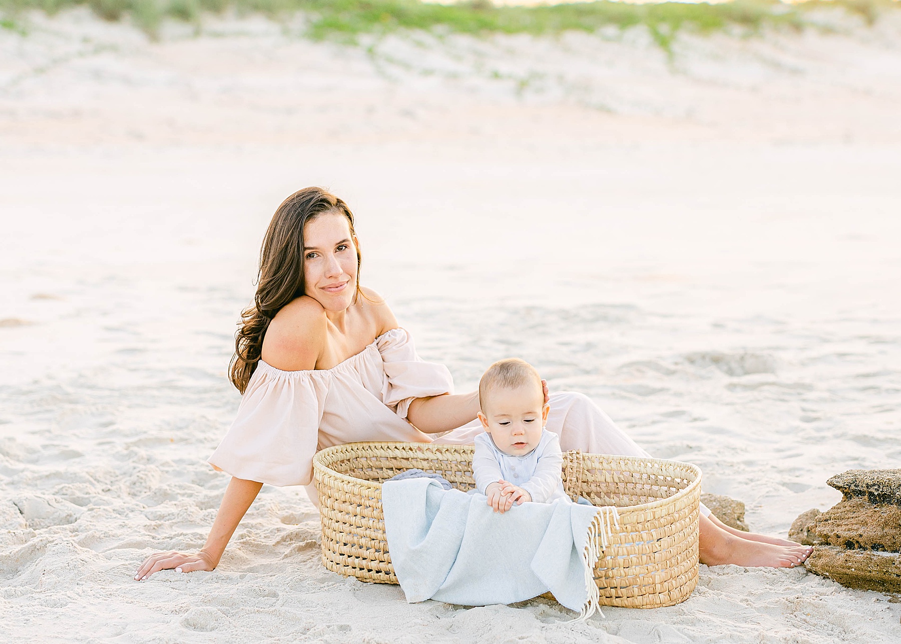 woman sitting with baby boy on the sand in blue blanket