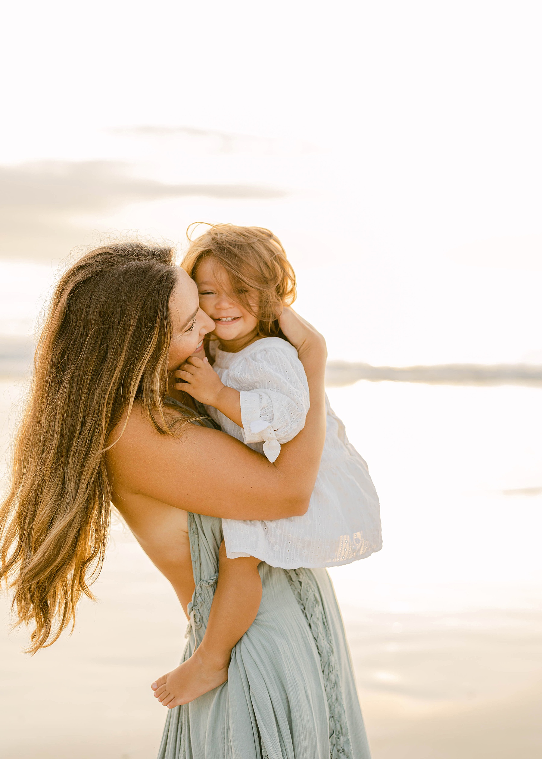 woman kissing little girl at sunrise on the beach