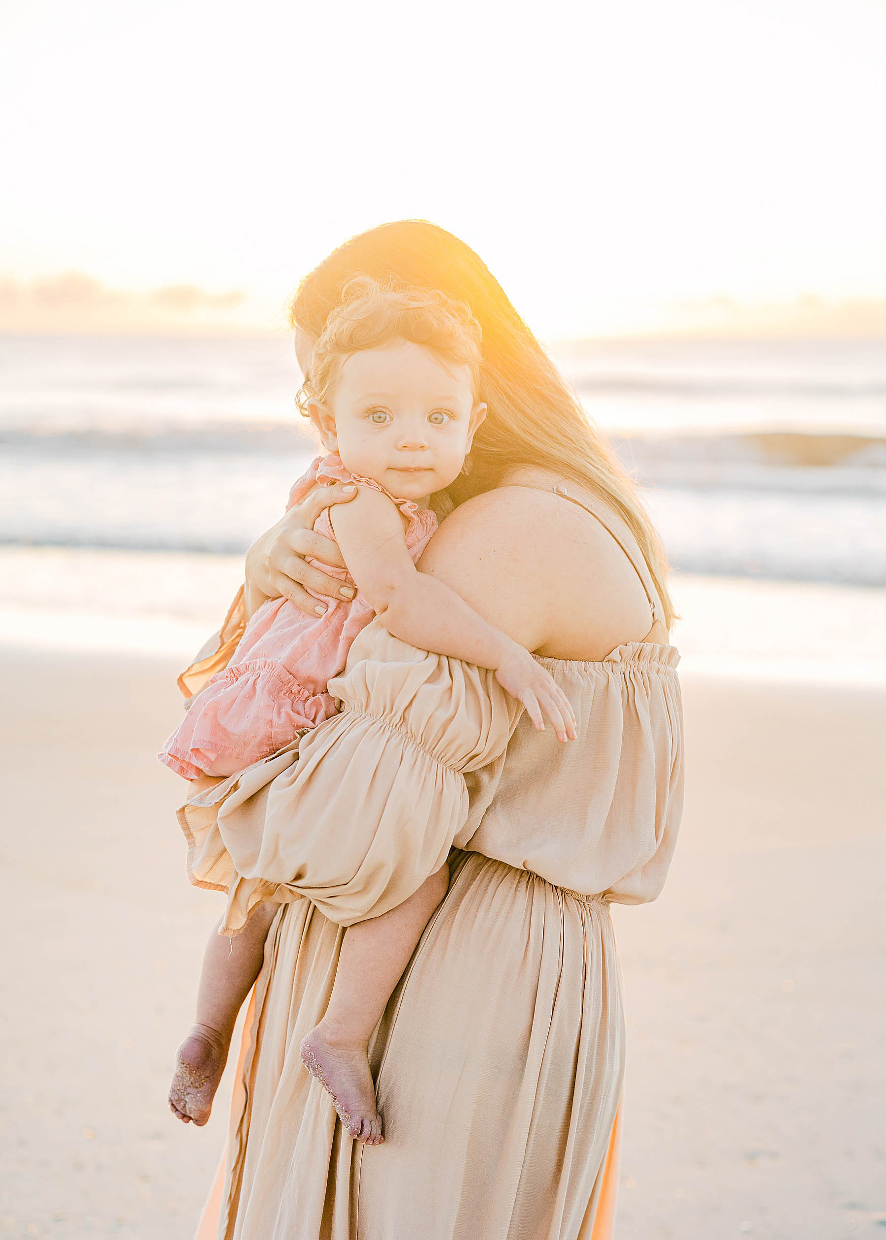 mom holding baby girl at sunrise on the beach wearing pink