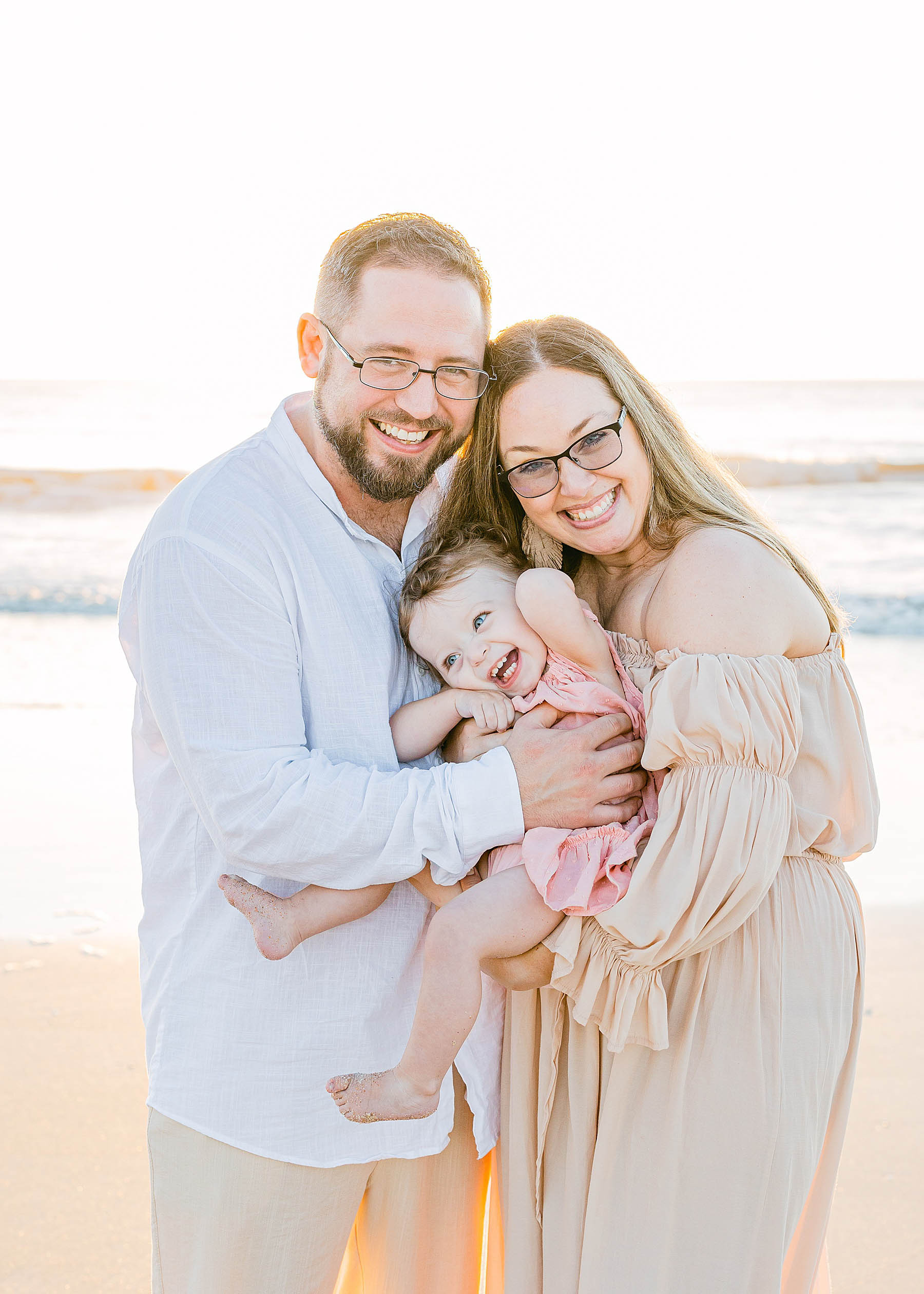 family holding baby girl on the beach at sunrise smiling