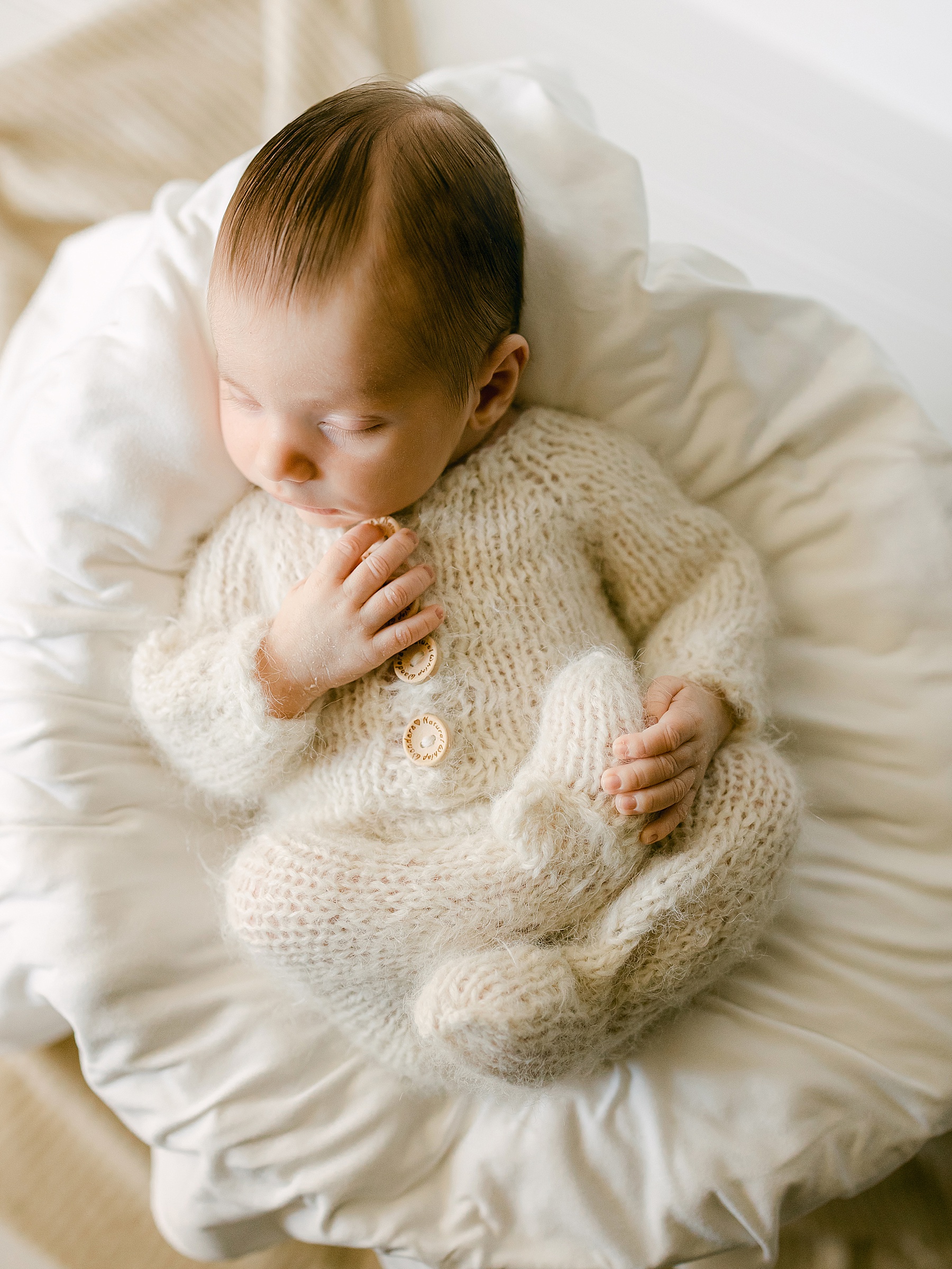 newborn baby boy sleeping in wicker basket wearing a wool outfit