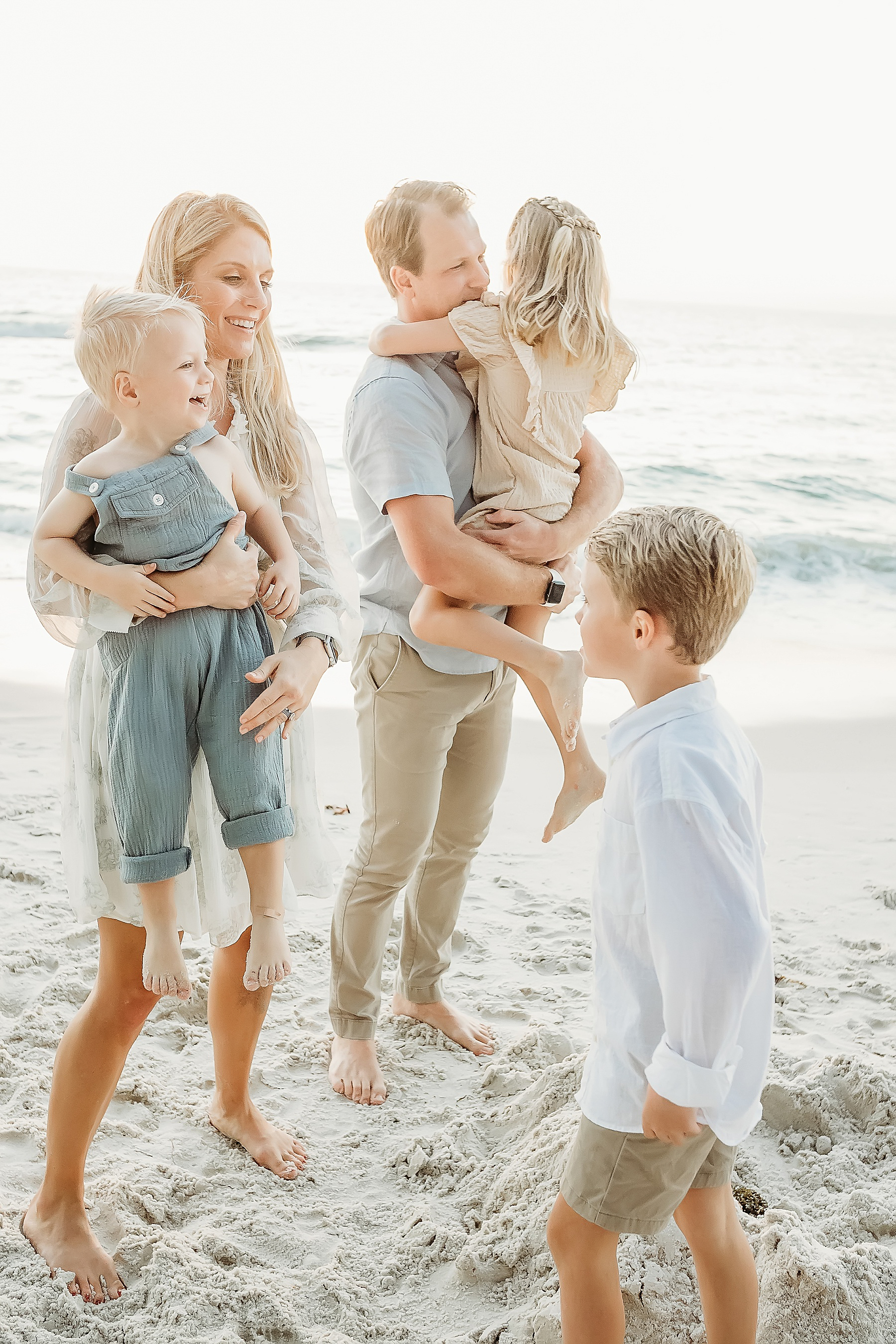 family holding each in neutral colors on the beach at sunset