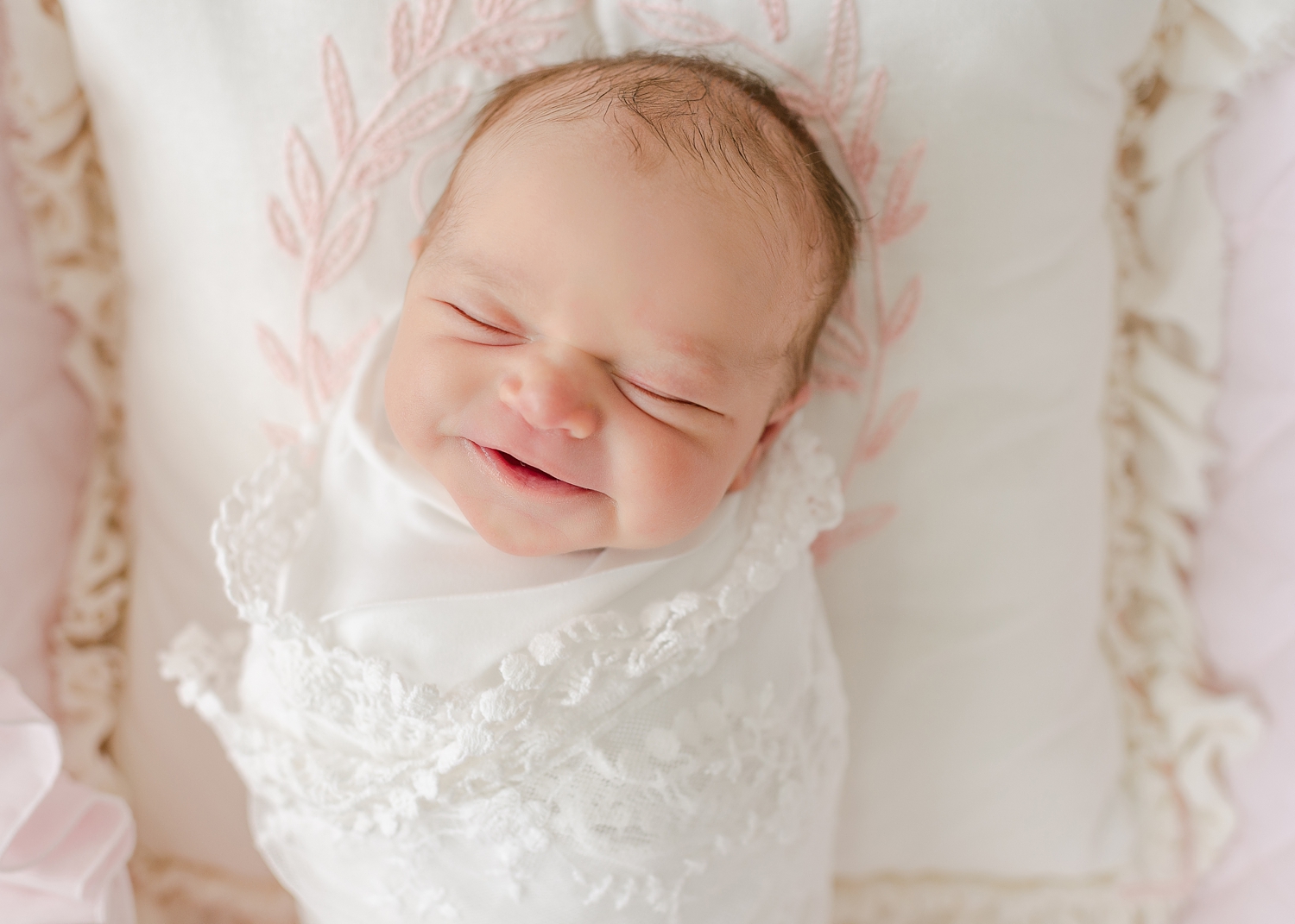 newborn baby girl wrapped in white lace blanket laying basket smiling
