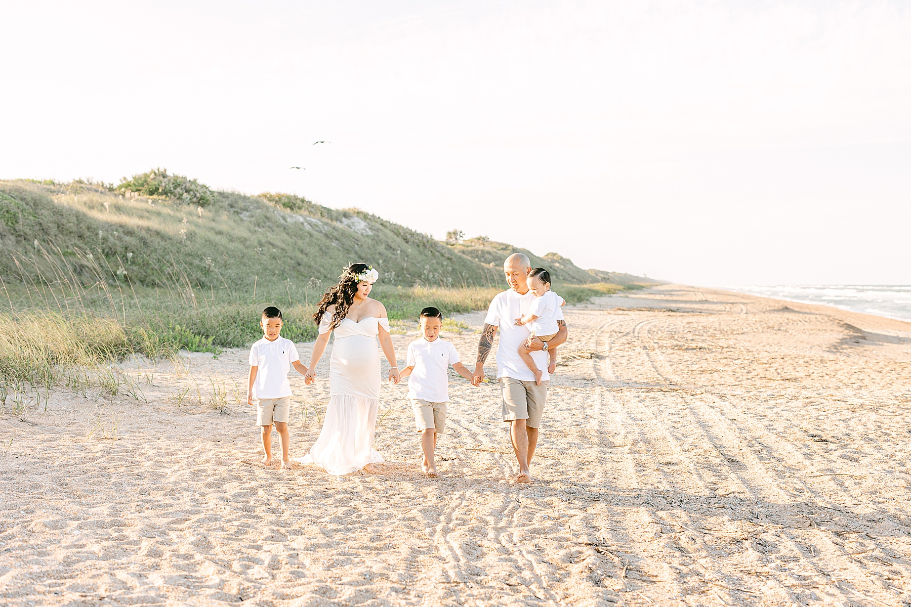 family walking on the beach at sunset holding hands wearing white