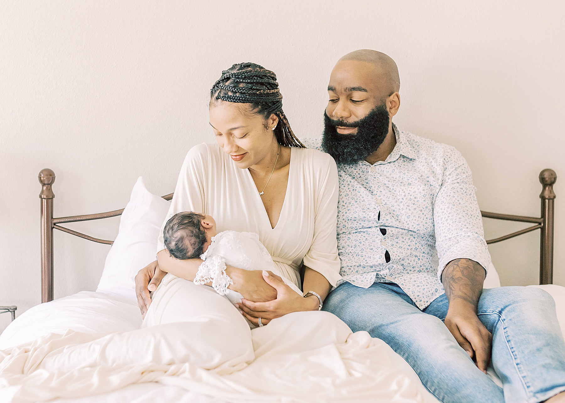 man and woman holding a baby girl on a bed in white sheets wearing neutral colors