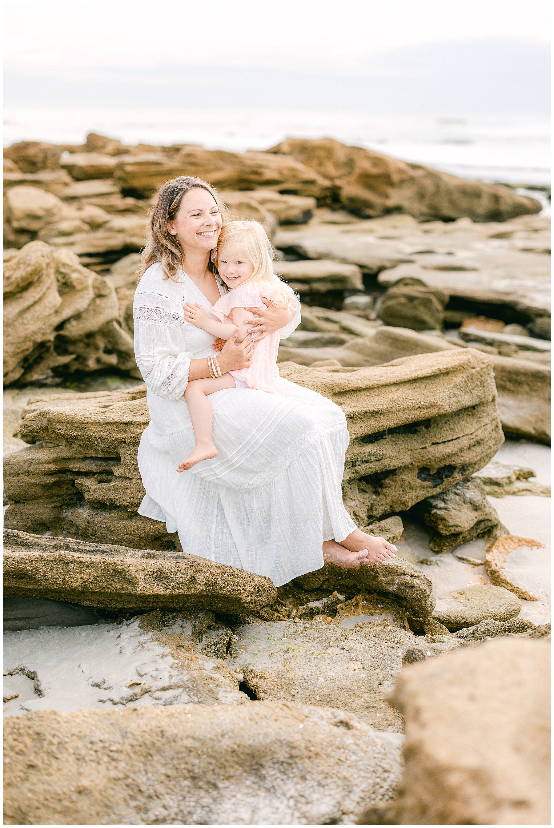 mom and little girl sitting together on the rocks laughing in florida