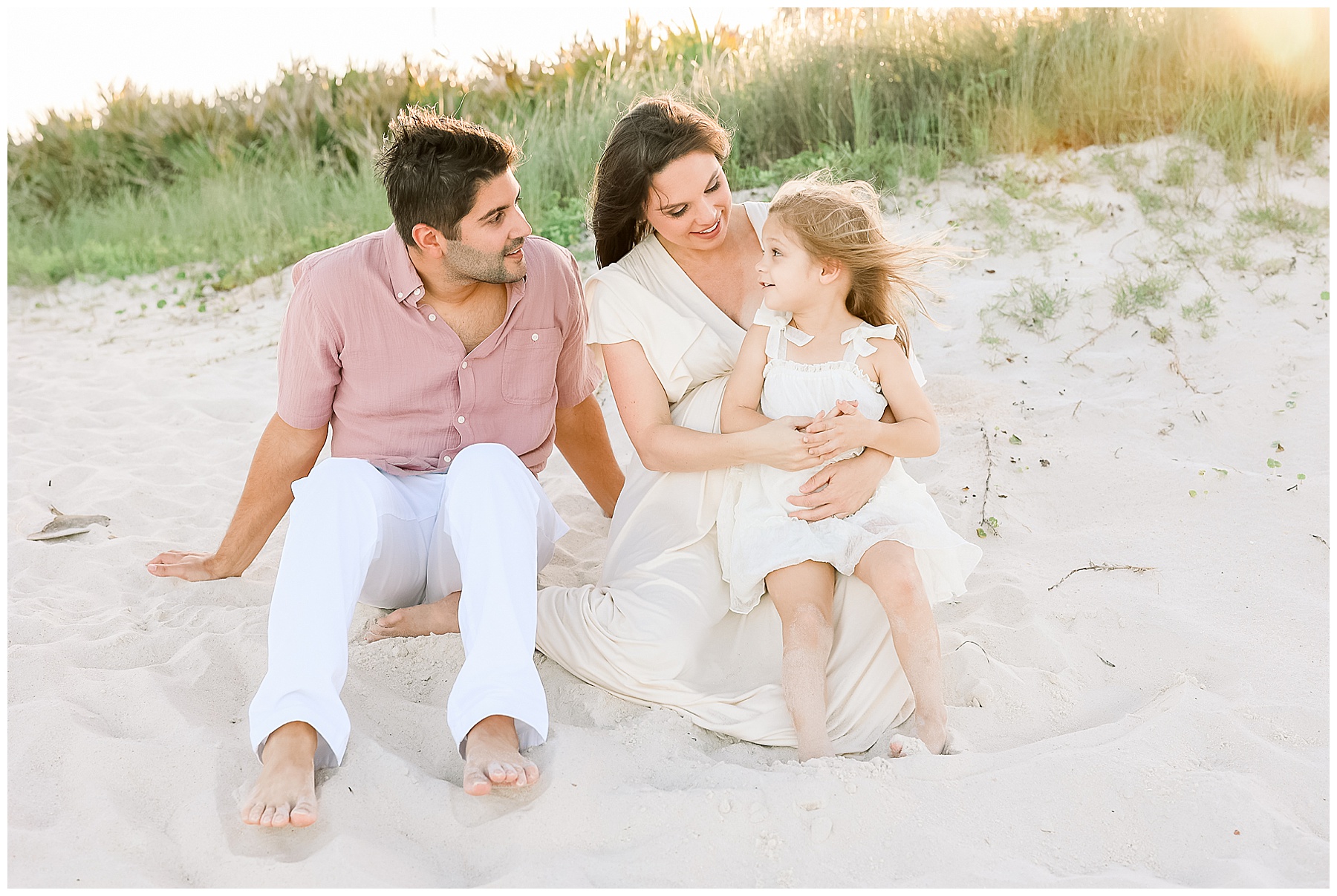 family of three sitting on the beach at sunset during golden hour in saint augustine florida