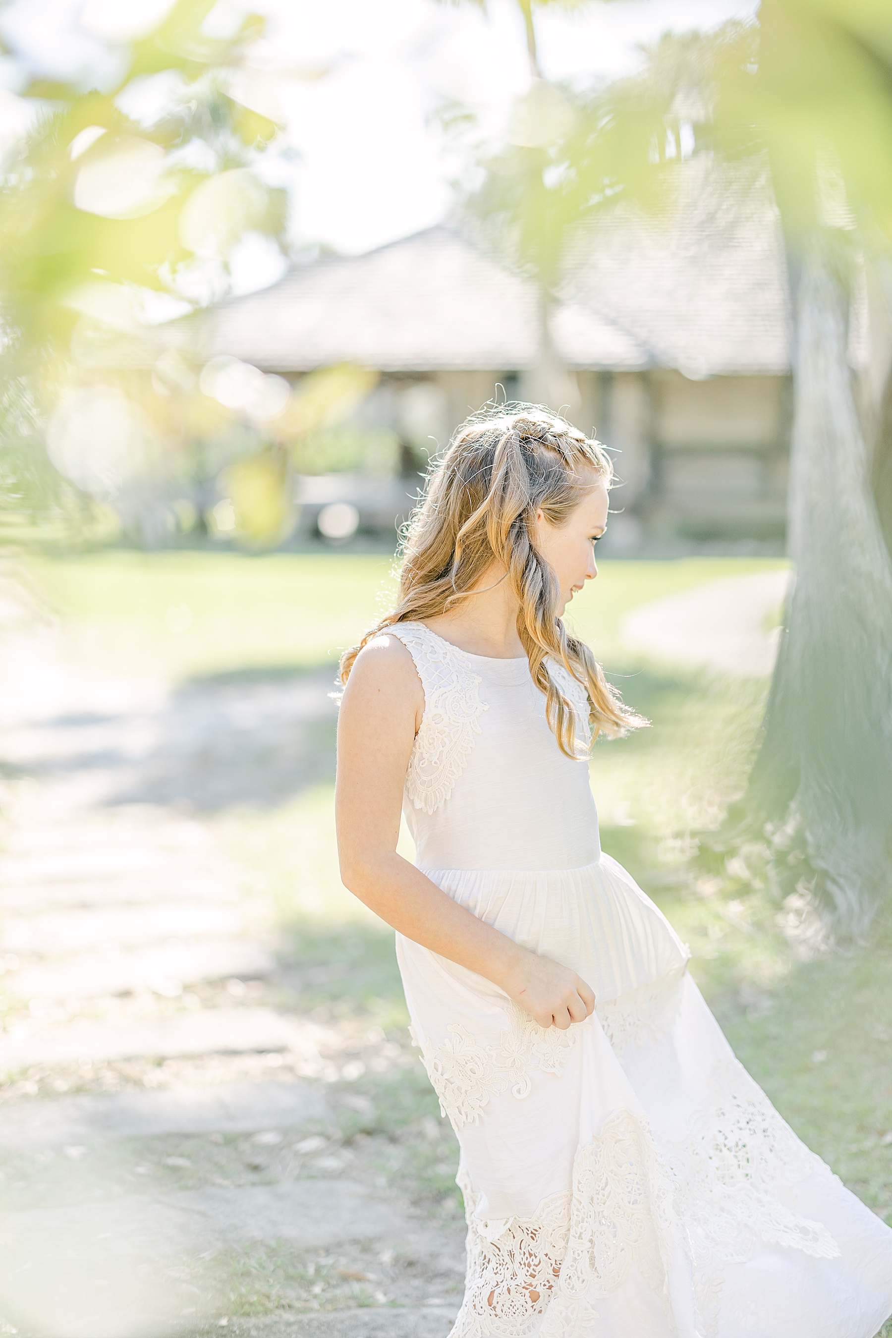 little girl in long white dress twirling in the sunlight on the grass