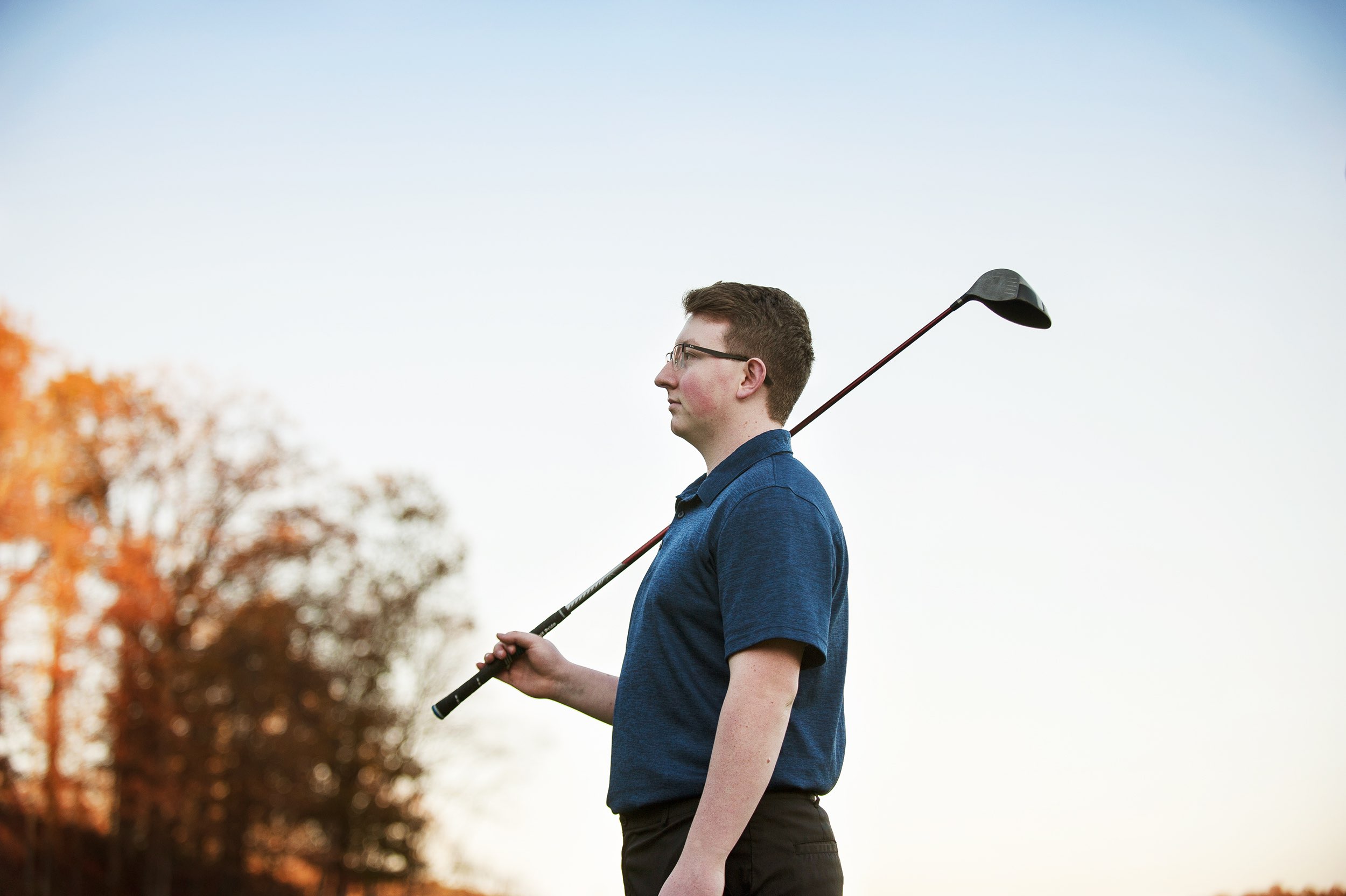 Close up of senior guy in blue shirt holding a golf club on his shoulder.