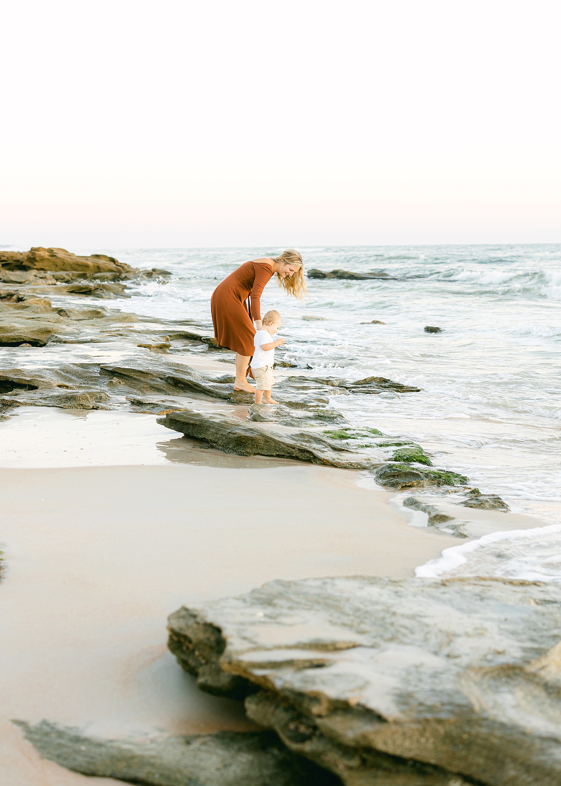 woman in rust colored dress standing in the water with little boy