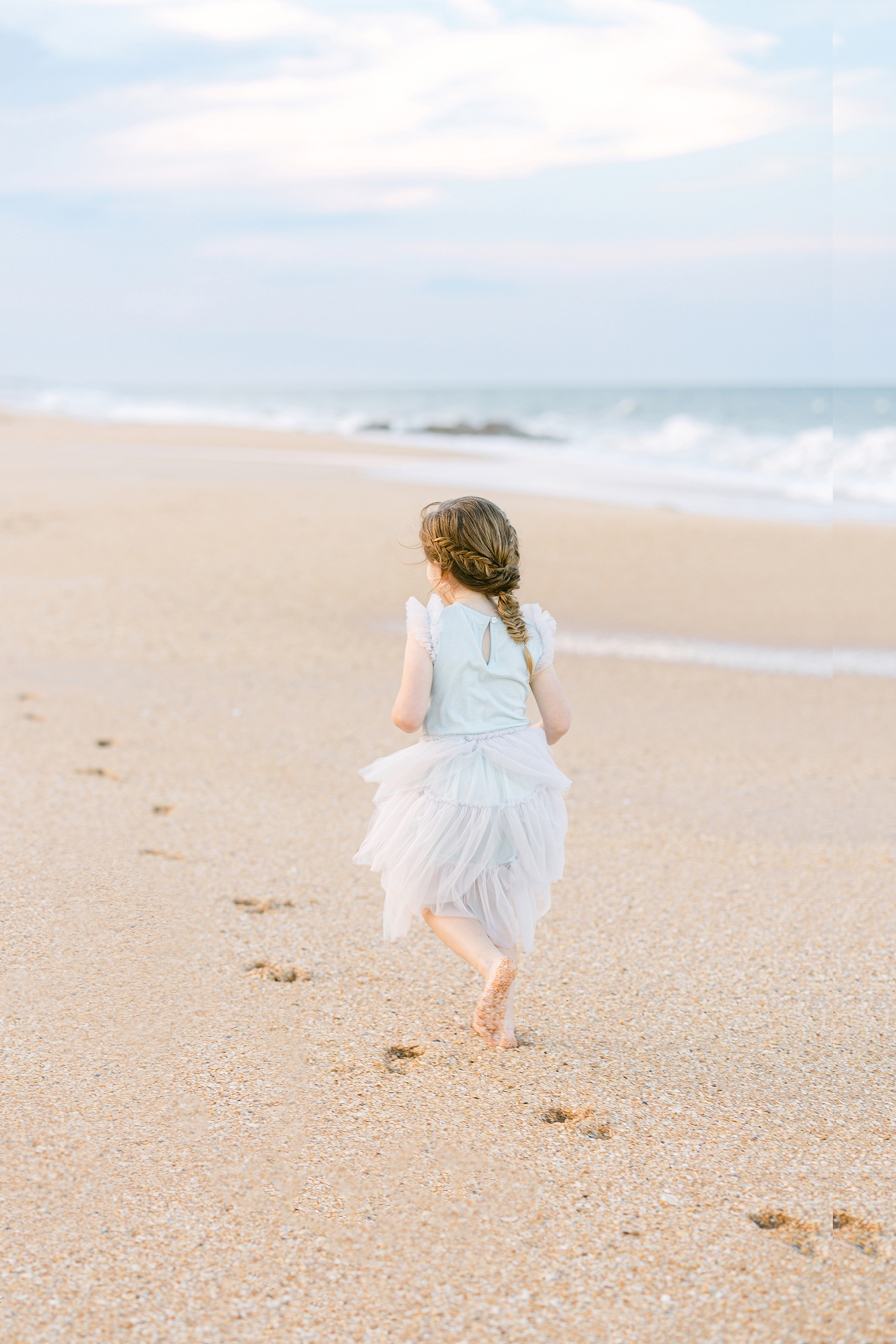 little girl in purple tutu dress running through the sand on the beach