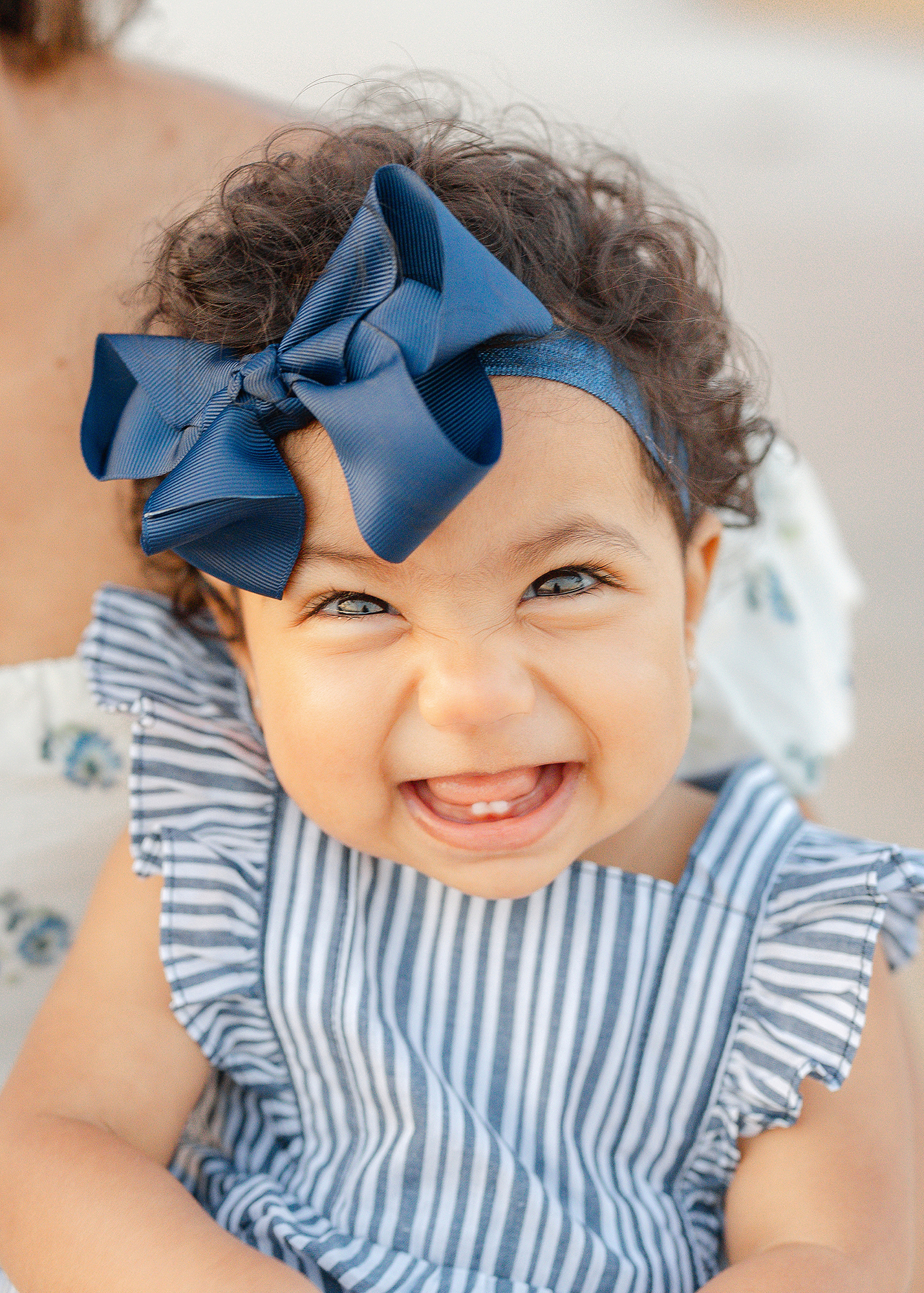 A smiling baby girl with two teeth in a blue and white striped romper with navy bow.
