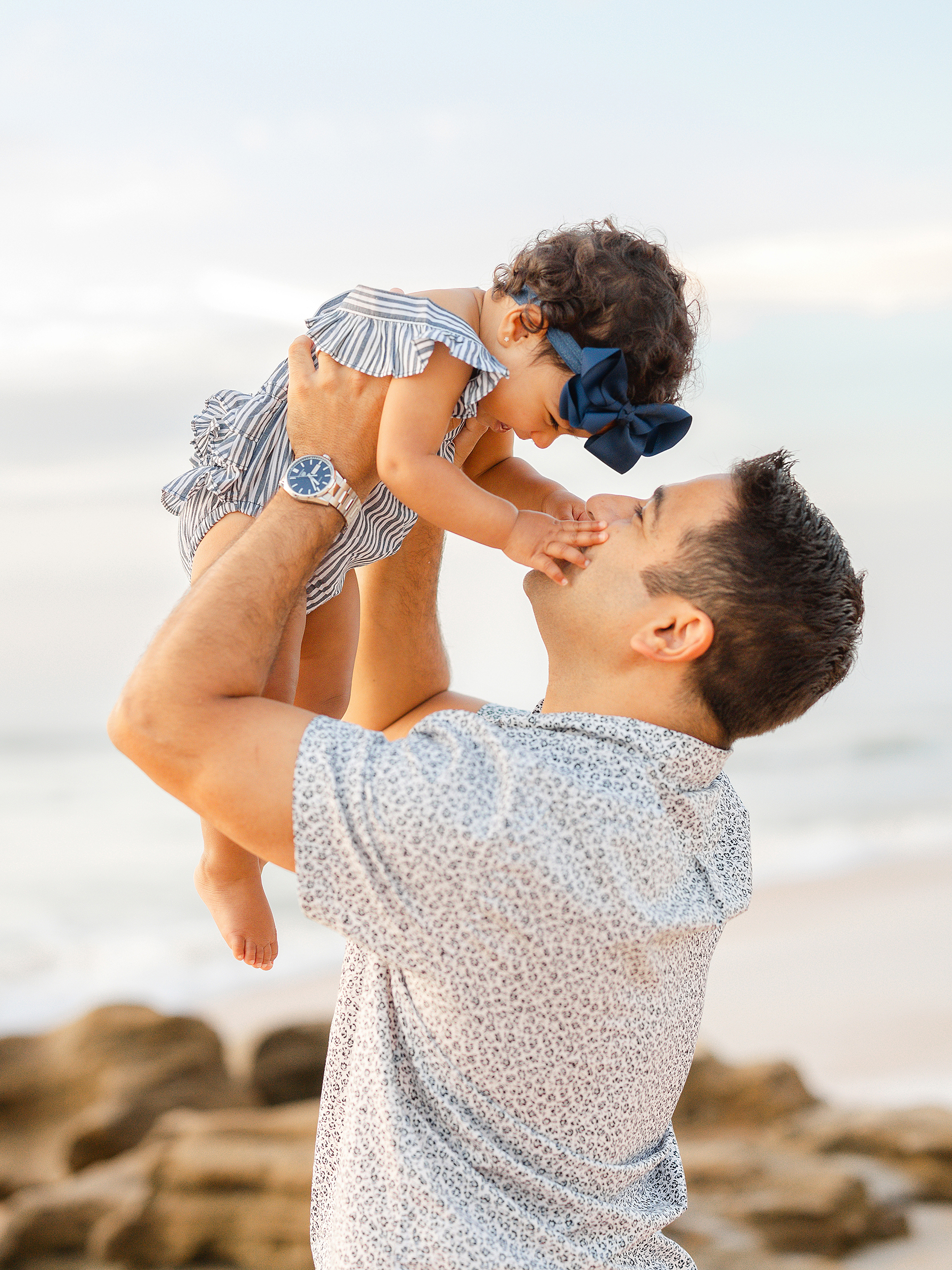A man holding baby girl in the air at the beach at sunrise