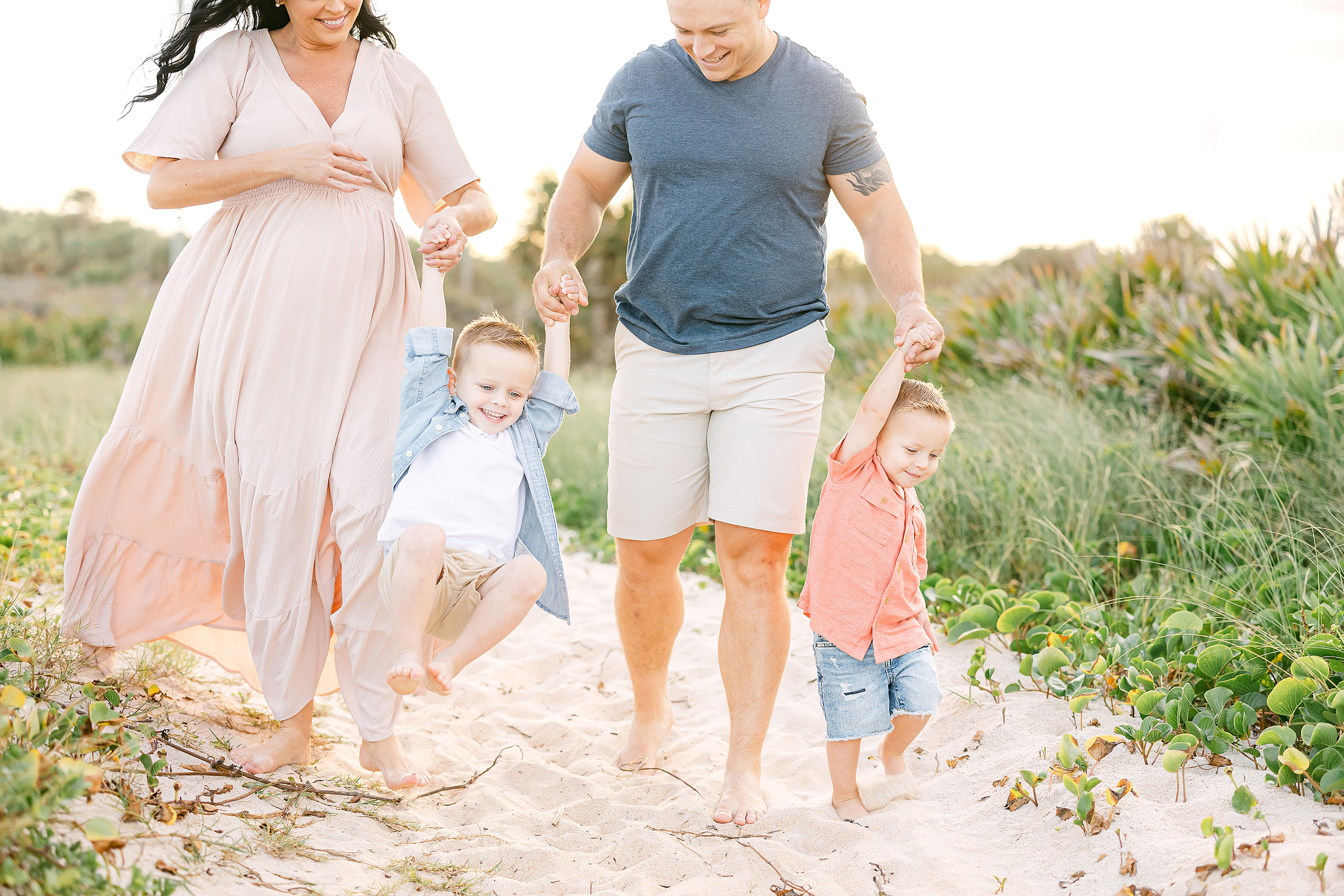 Light and airy maternity portrait of a family on the beach at sunset.