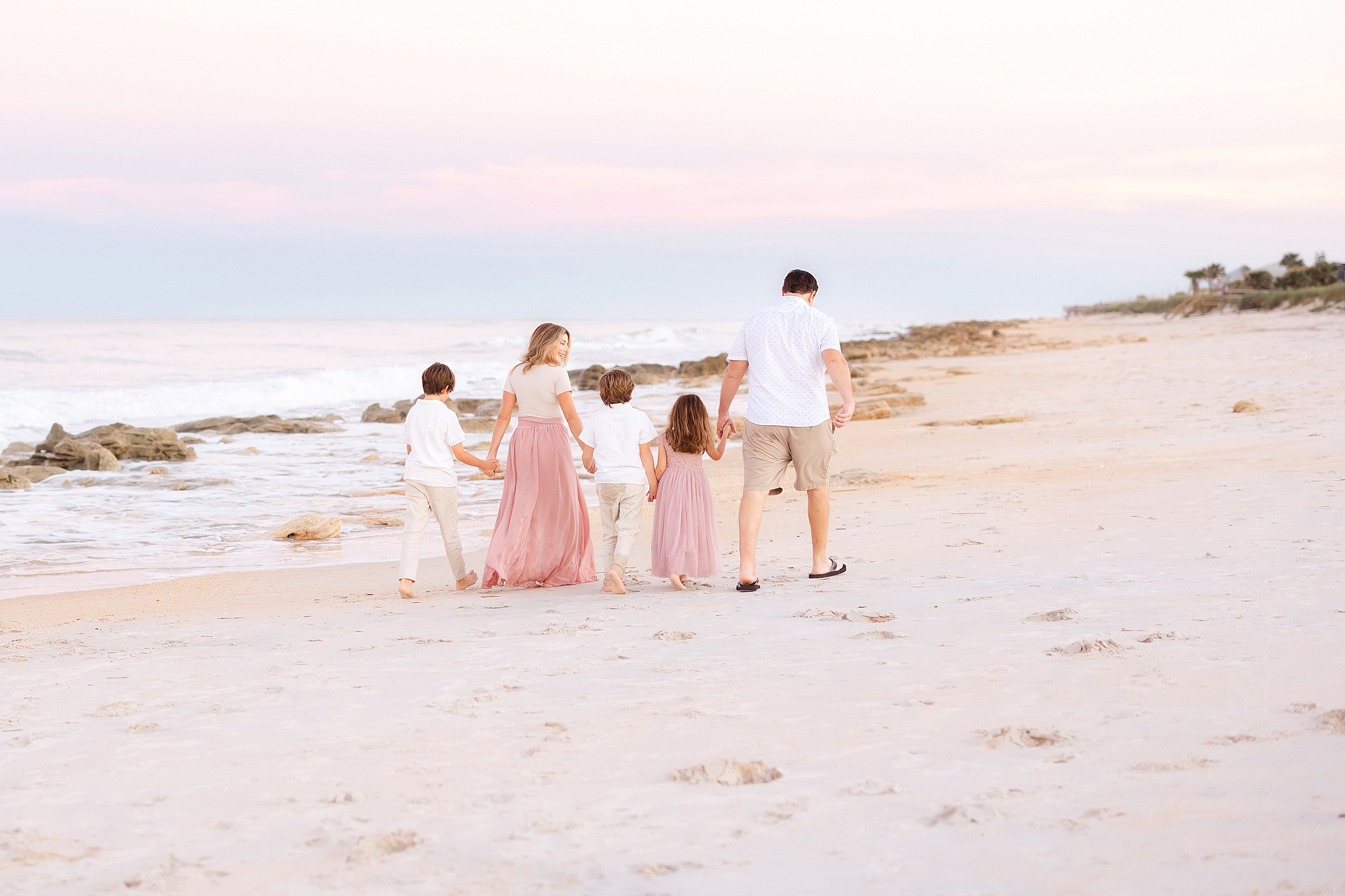 A family walking on the beach in St. Augustine at sunset with pastel pink skies.