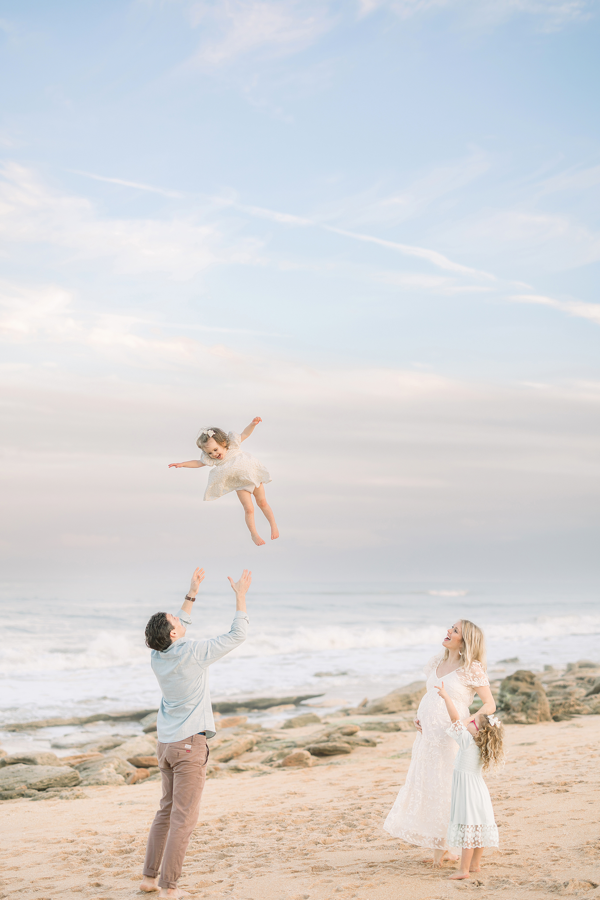 A family of four throwing a little girl up in the air on the beach at sunset.