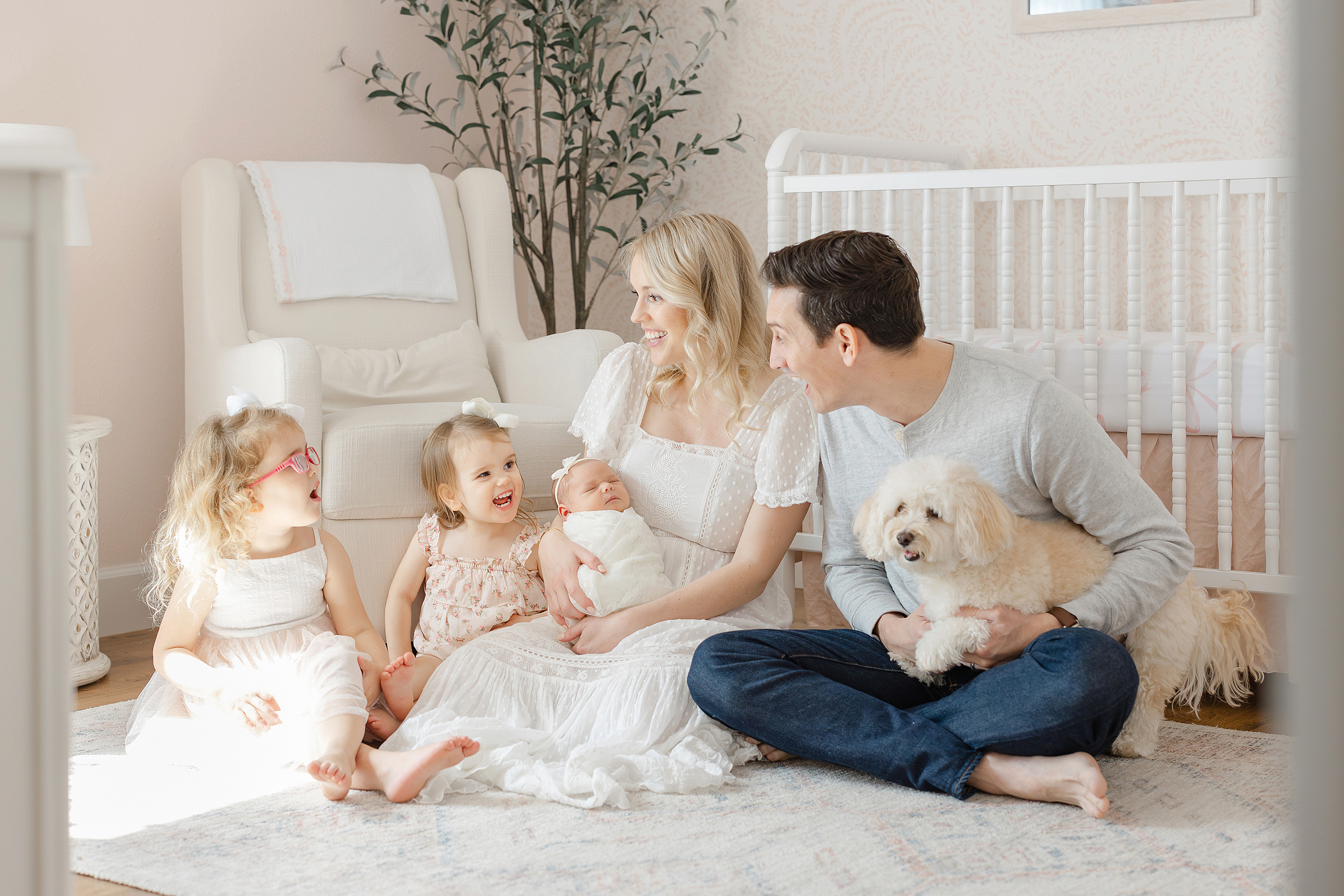 An in home newborn portrait of a family of five sitting on the floor in their third baby girl's nursery.